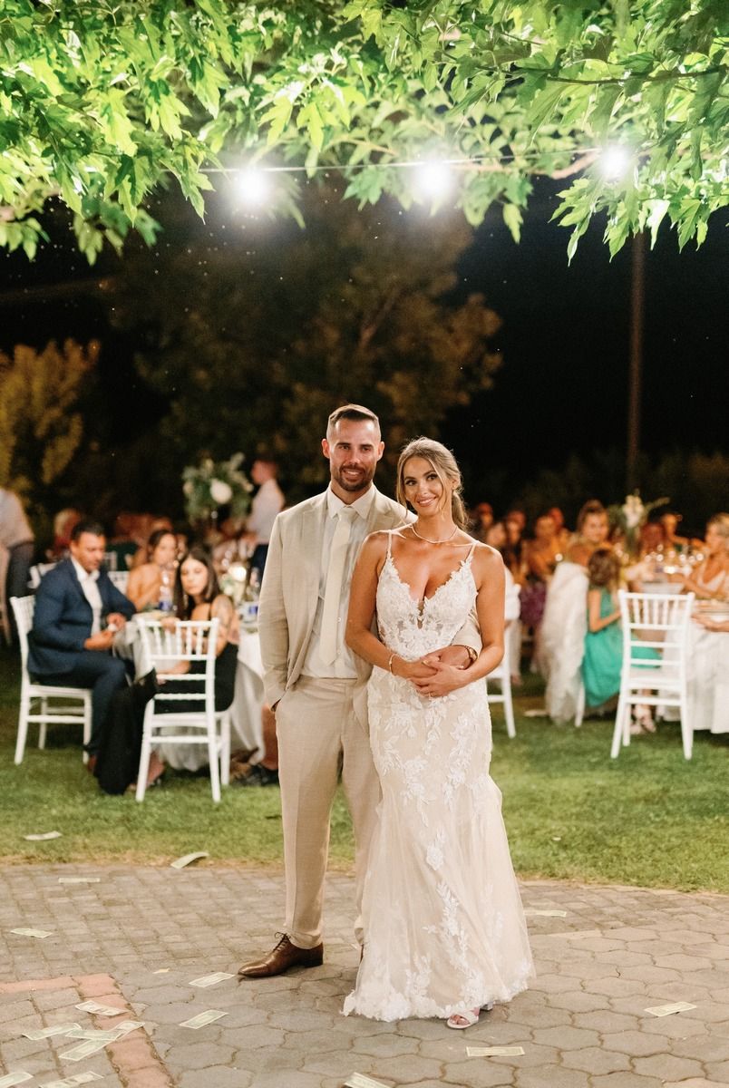 Newlyweds pose together on brick patio under string lights at outdoor garden reception.