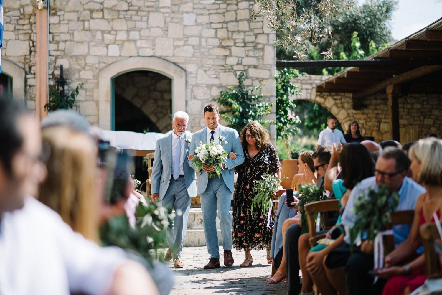 Wedding ceremony processional at a rustic stone venue with garden surroundings.