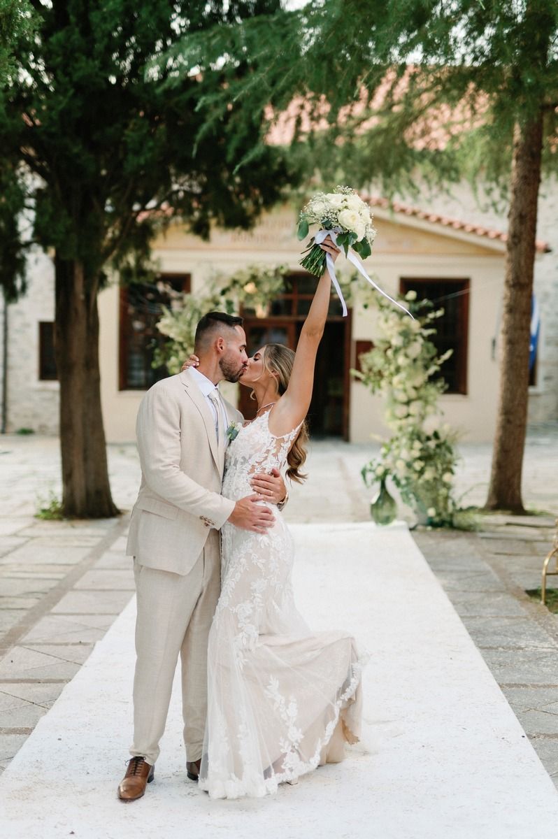 Joyful newlyweds celebrate on white aisle runner with bride holding bouquet high in celebration.