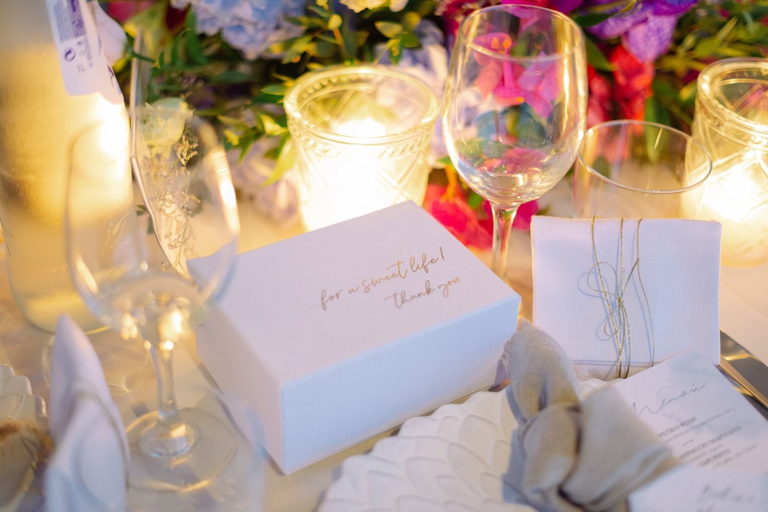 Close-up of wedding table place cards illuminated by candlelight with wine glasses.