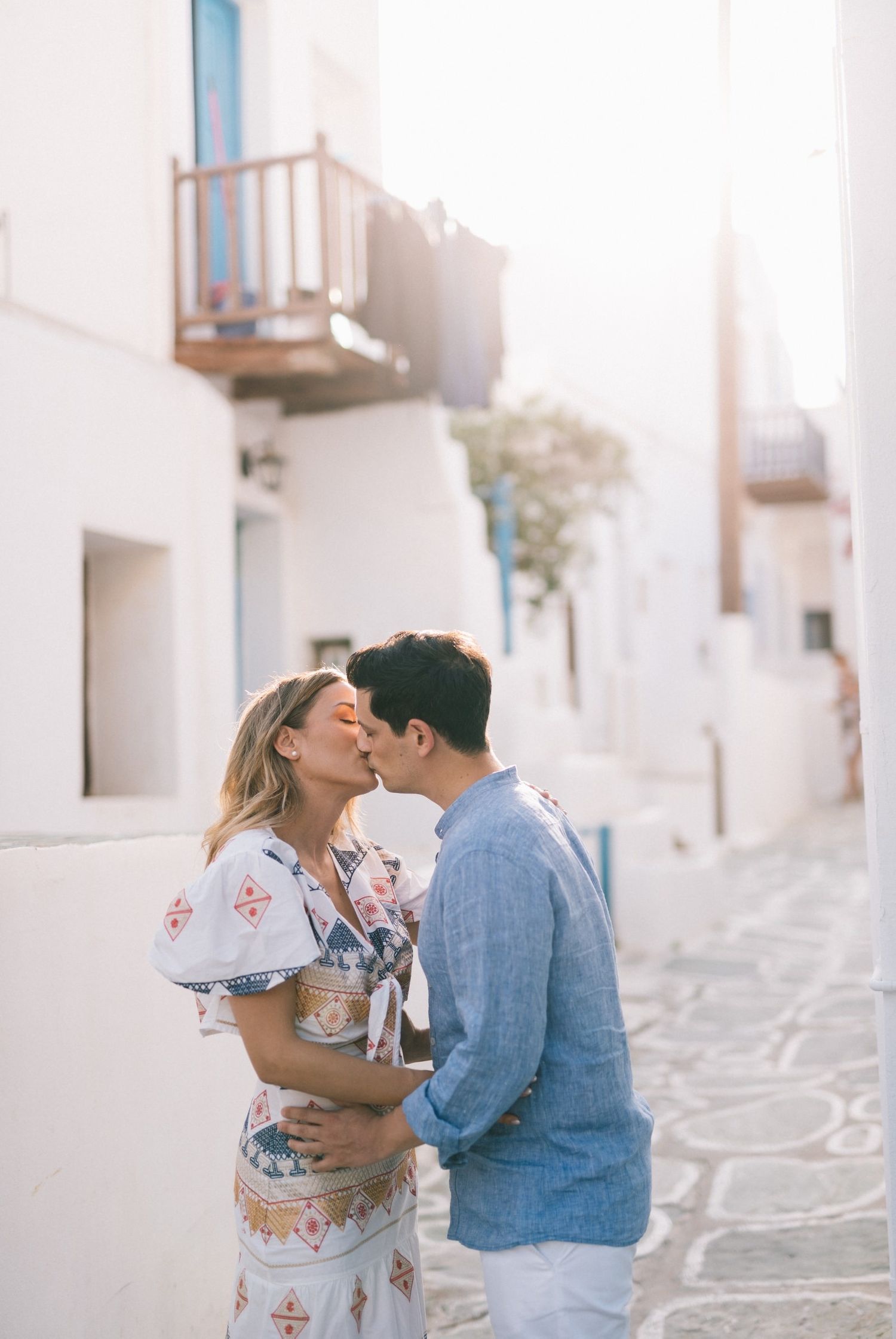 A tender embrace in a charming white-washed Mediterranean street with blue accents.