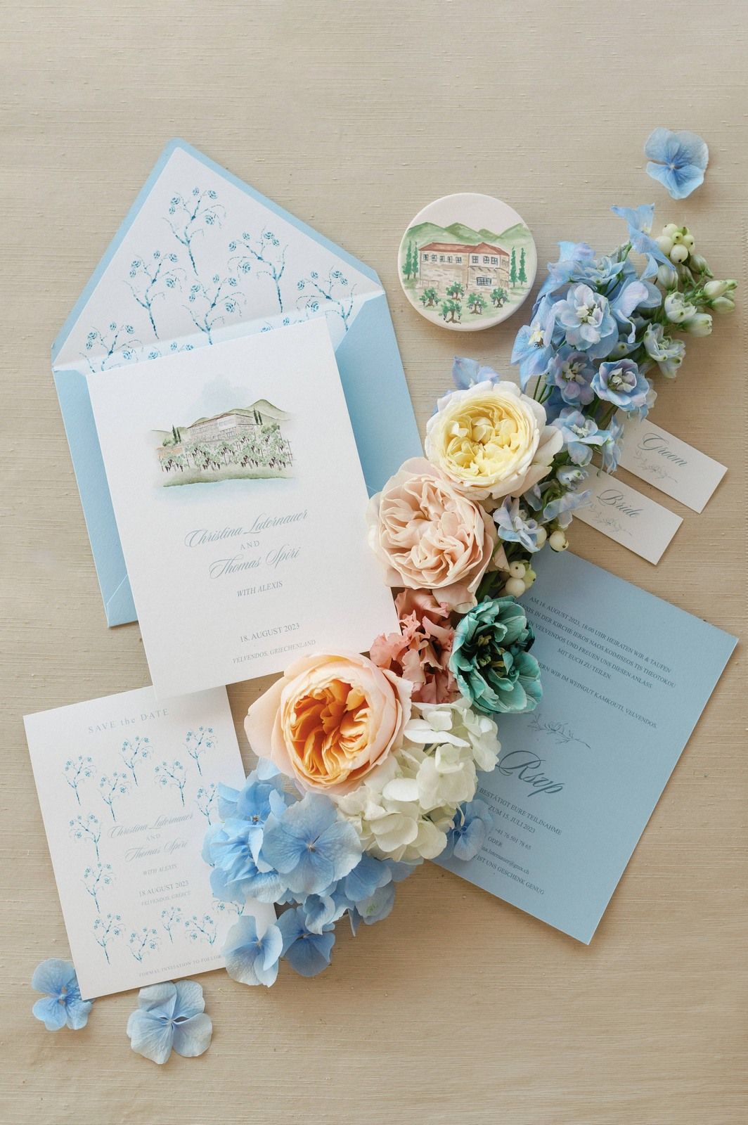 Wedding stationery in soft blue and peach tones with floral accents arranged on a light wooden surface.