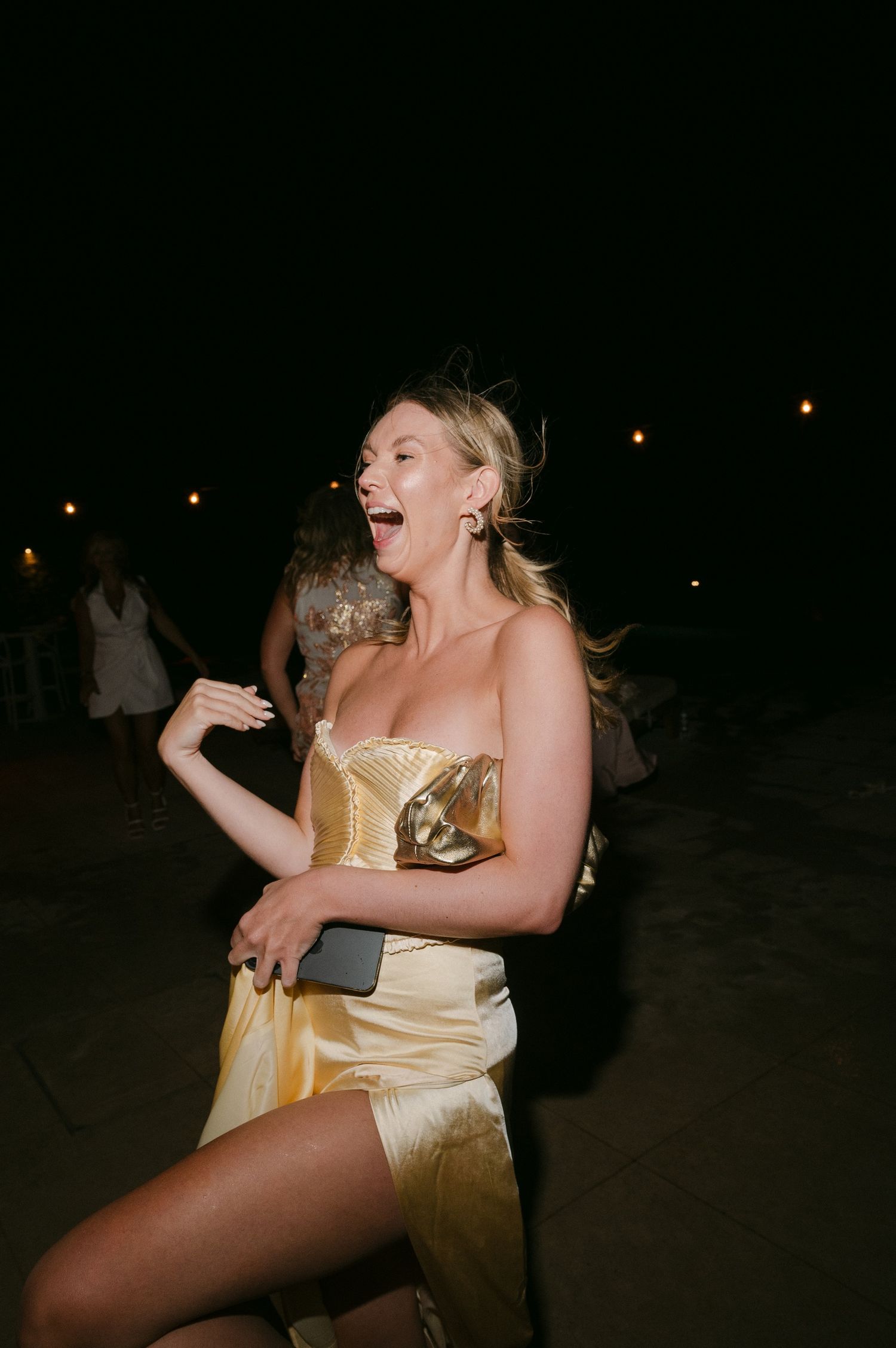 A person in a gold dress dances joyfully at a nighttime event.