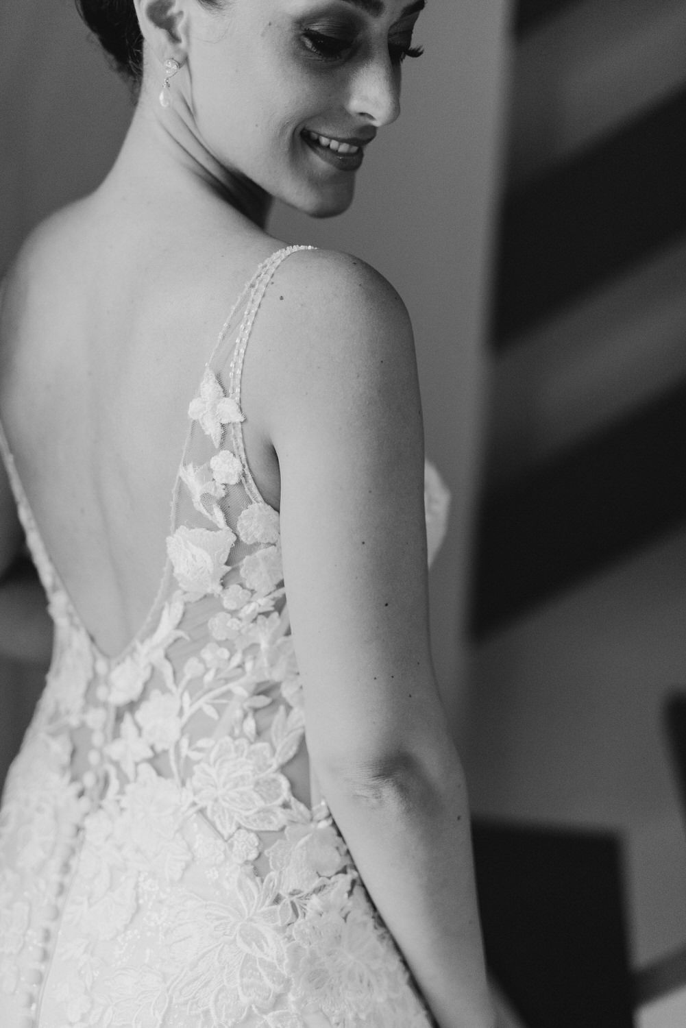 Black and white detail shot of a lace wedding dress with delicate floral appliques and open back design.