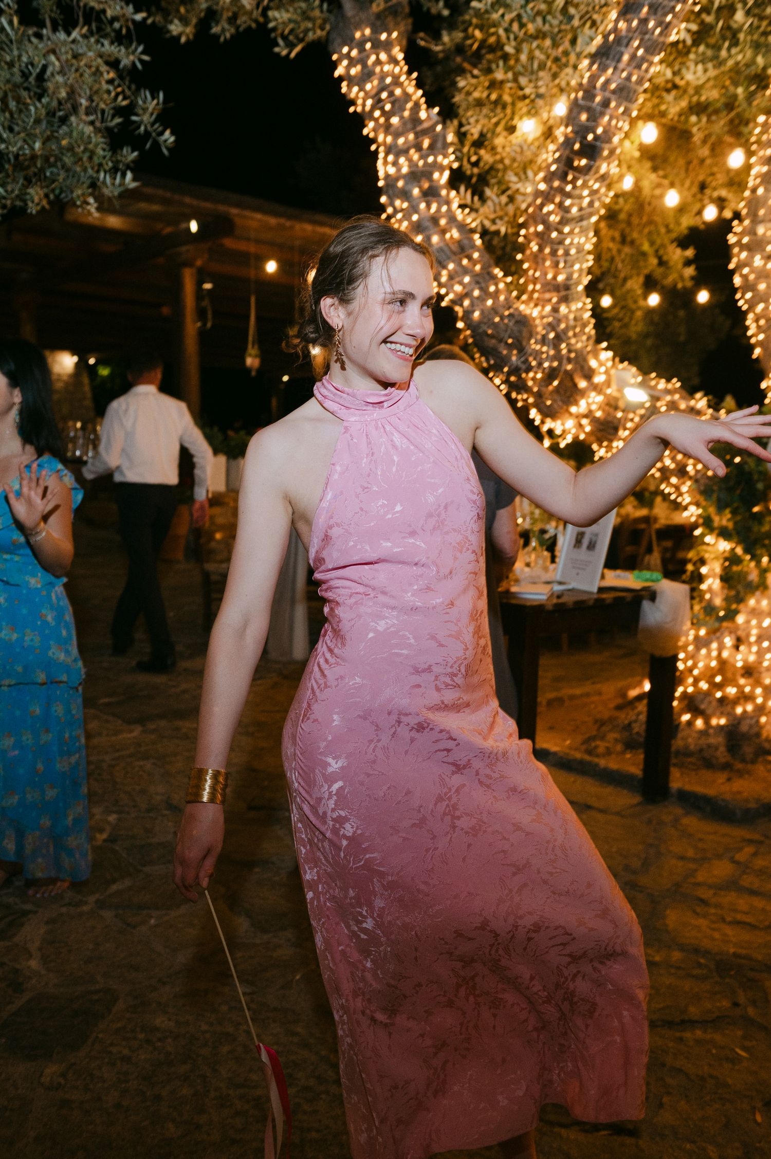 A person in a pink dress dancing at an outdoor evening party with twinkling lights decorating trees in the background.
