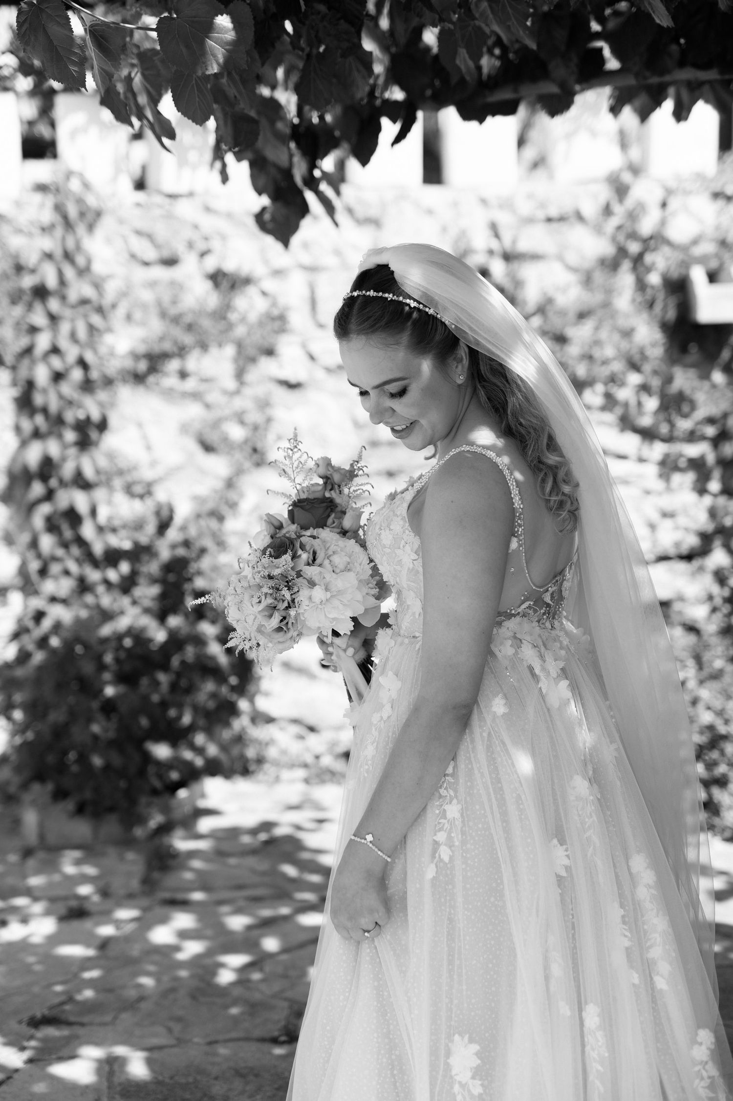 Black and white photo series of a bride in a flowy wedding dress with delicate details standing in dappled sunlight.