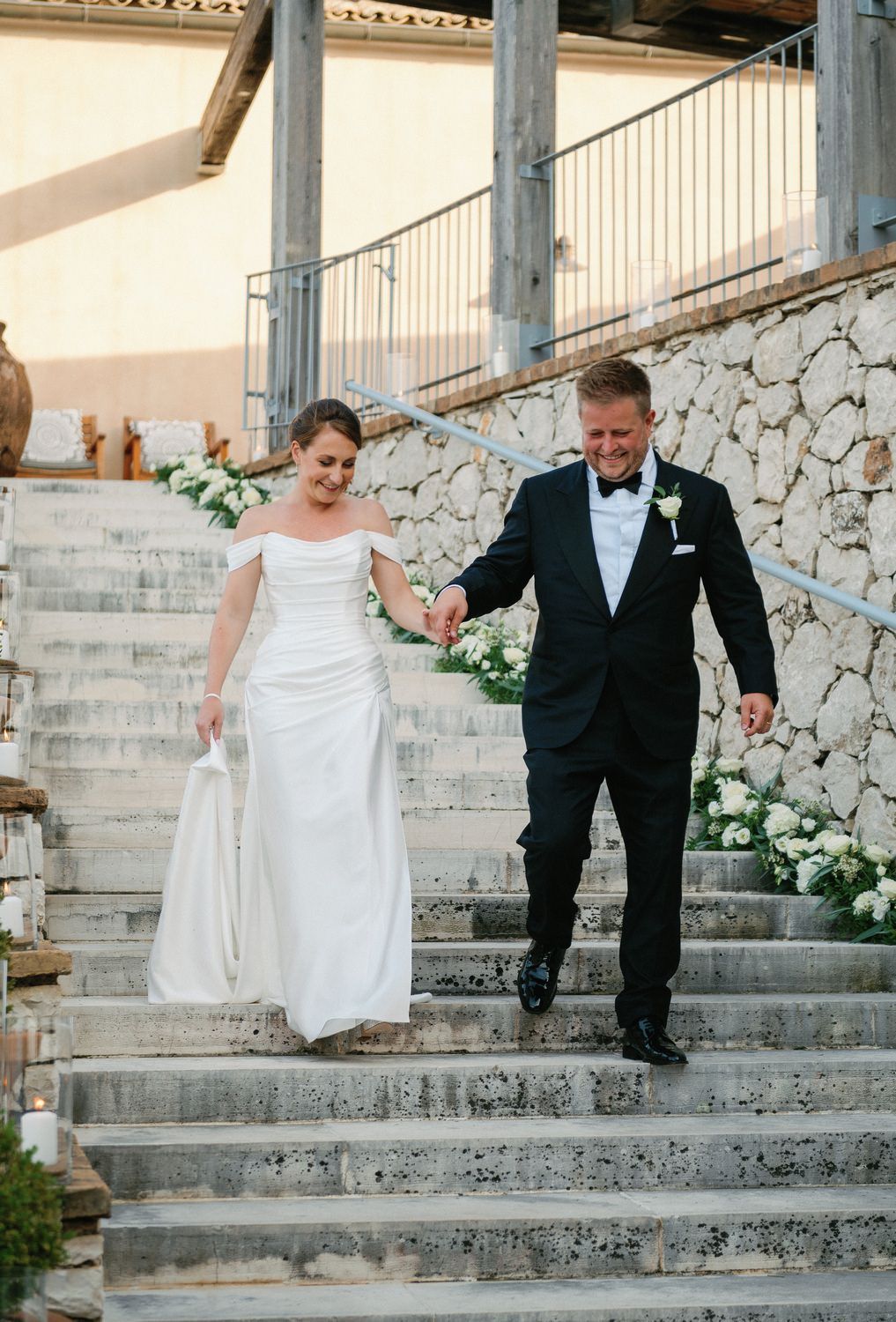 Newlyweds carefully walking down stone steps at an outdoor venue.