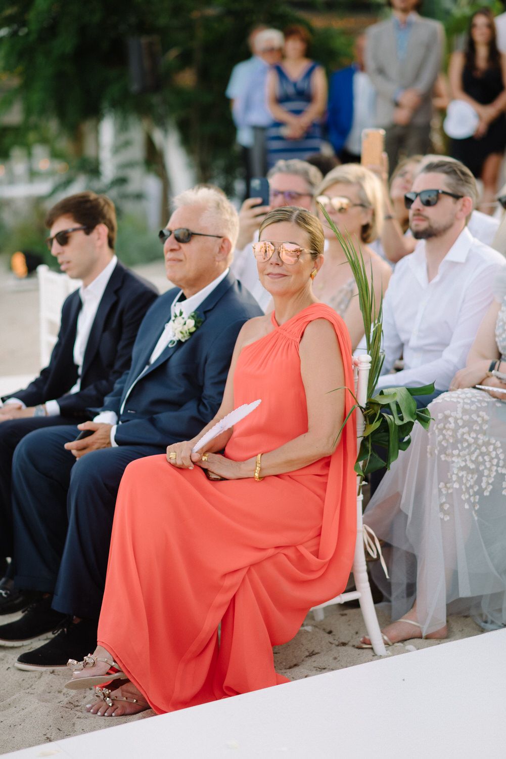 Wedding guests seated in formal attire during outdoor ceremony.