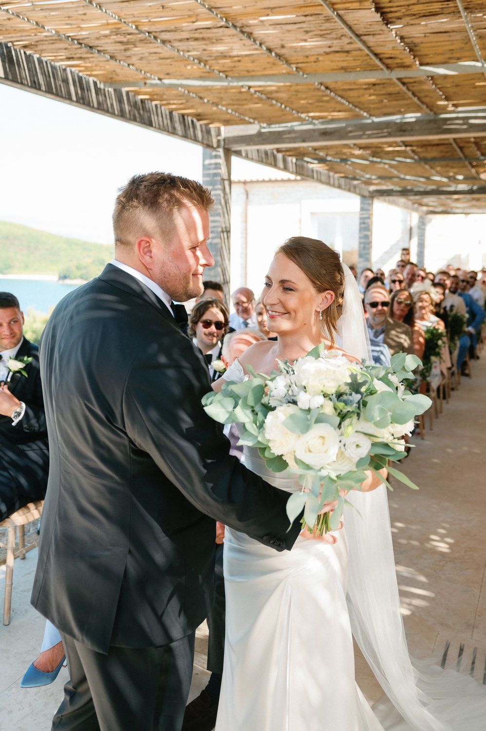 Wedding couple sharing moment during ceremony under rustic bamboo pergola.