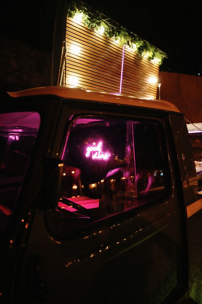 Vintage vehicle with illuminated neon signage and decorative lights at night event.