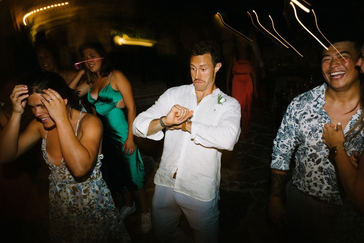 Party guests dancing and laughing together in a dimly lit venue with festive lighting.