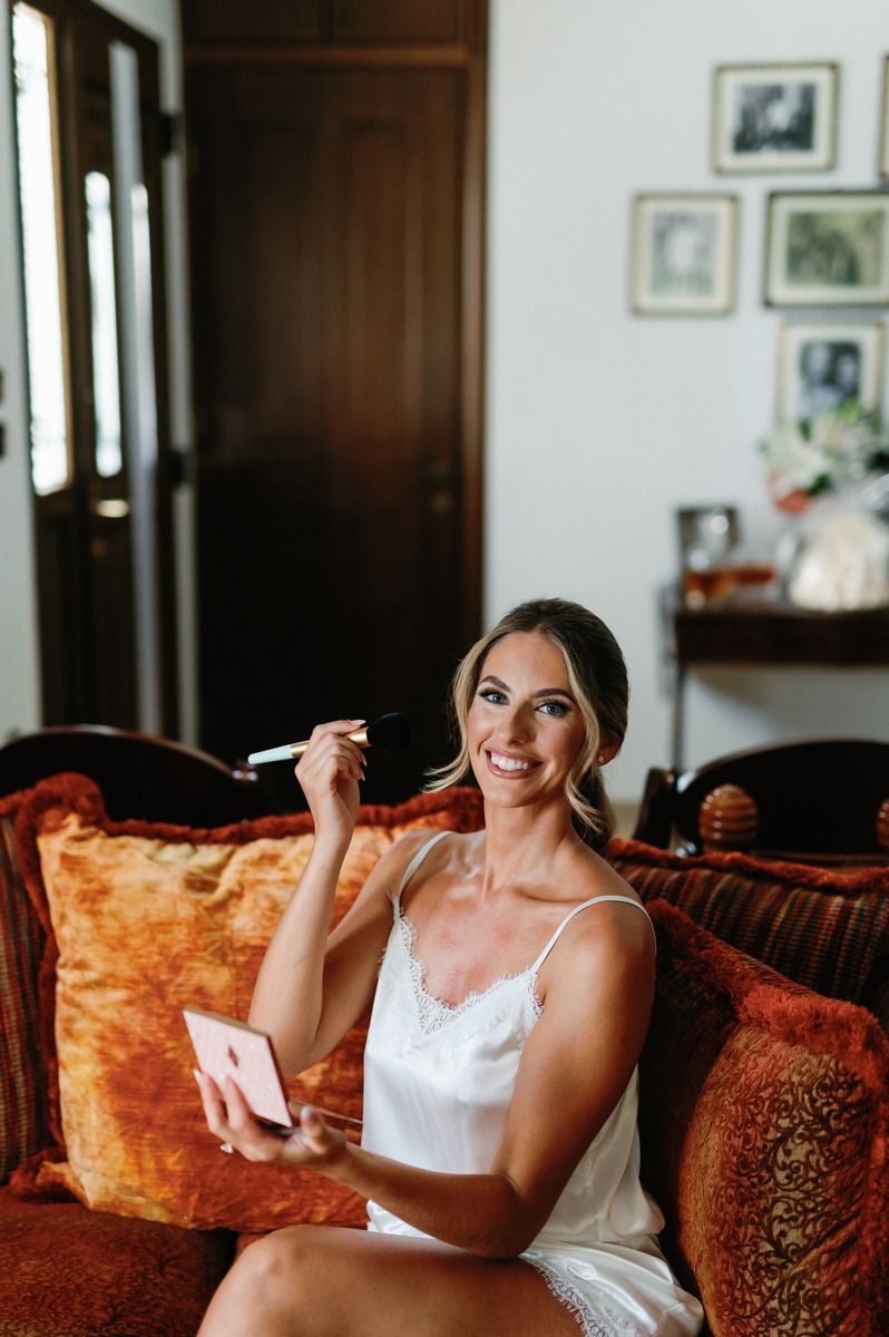 Wedding preparation scene with someone getting makeup done while sitting on an orange velvet couch.