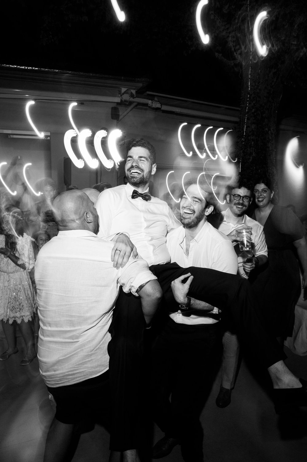 A black and white party photo showing people celebrating with neon lights in the background at a festive gathering.