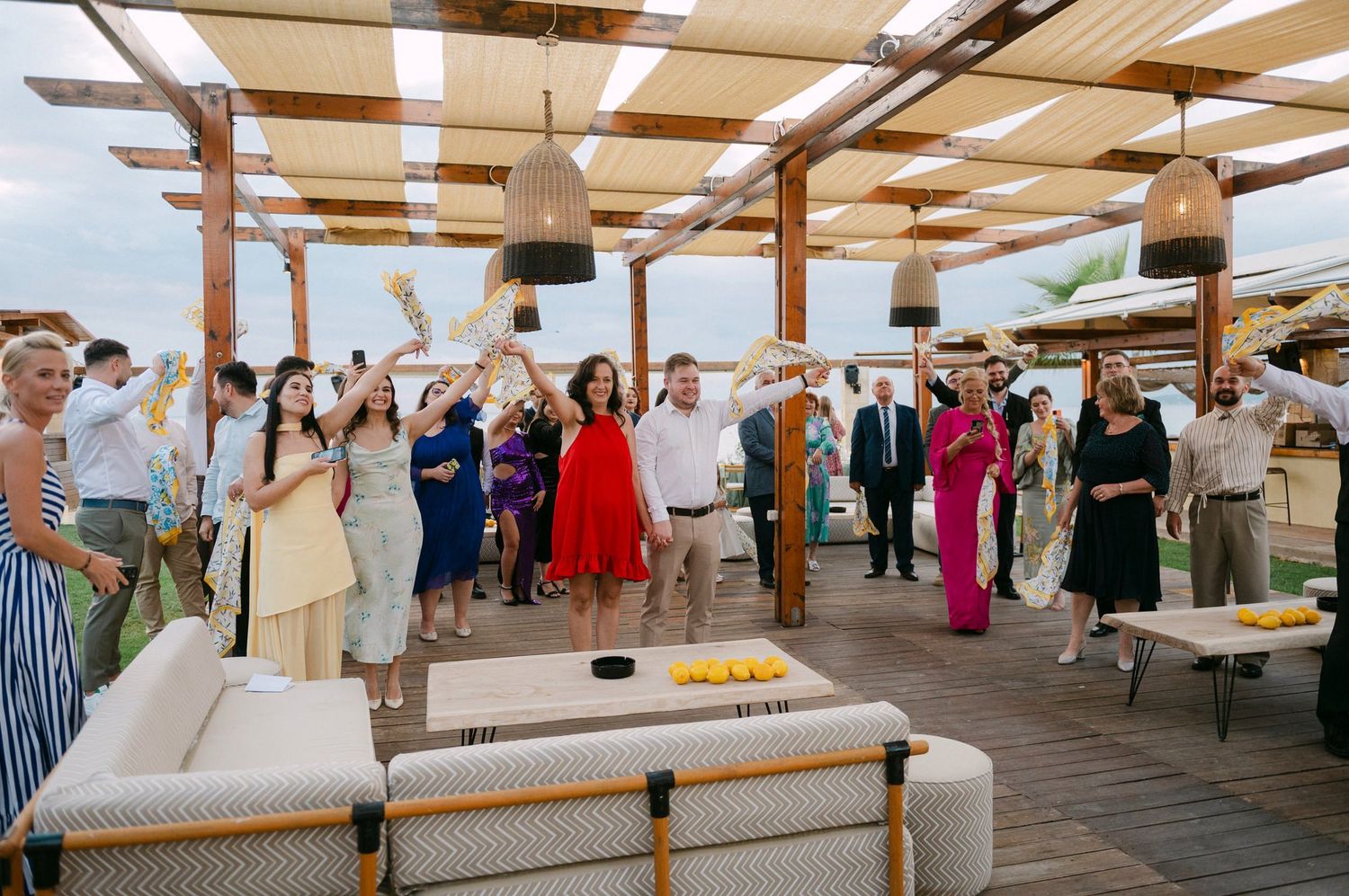 People gather at a covered outdoor venue with wooden beams and long tables set up for a community event.
