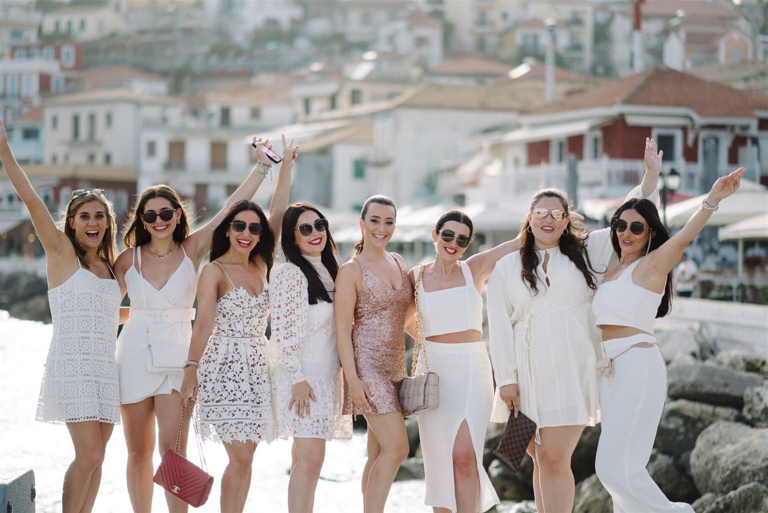 A group of women in white dresses pose together on a seaside dock during a wedding celebration.