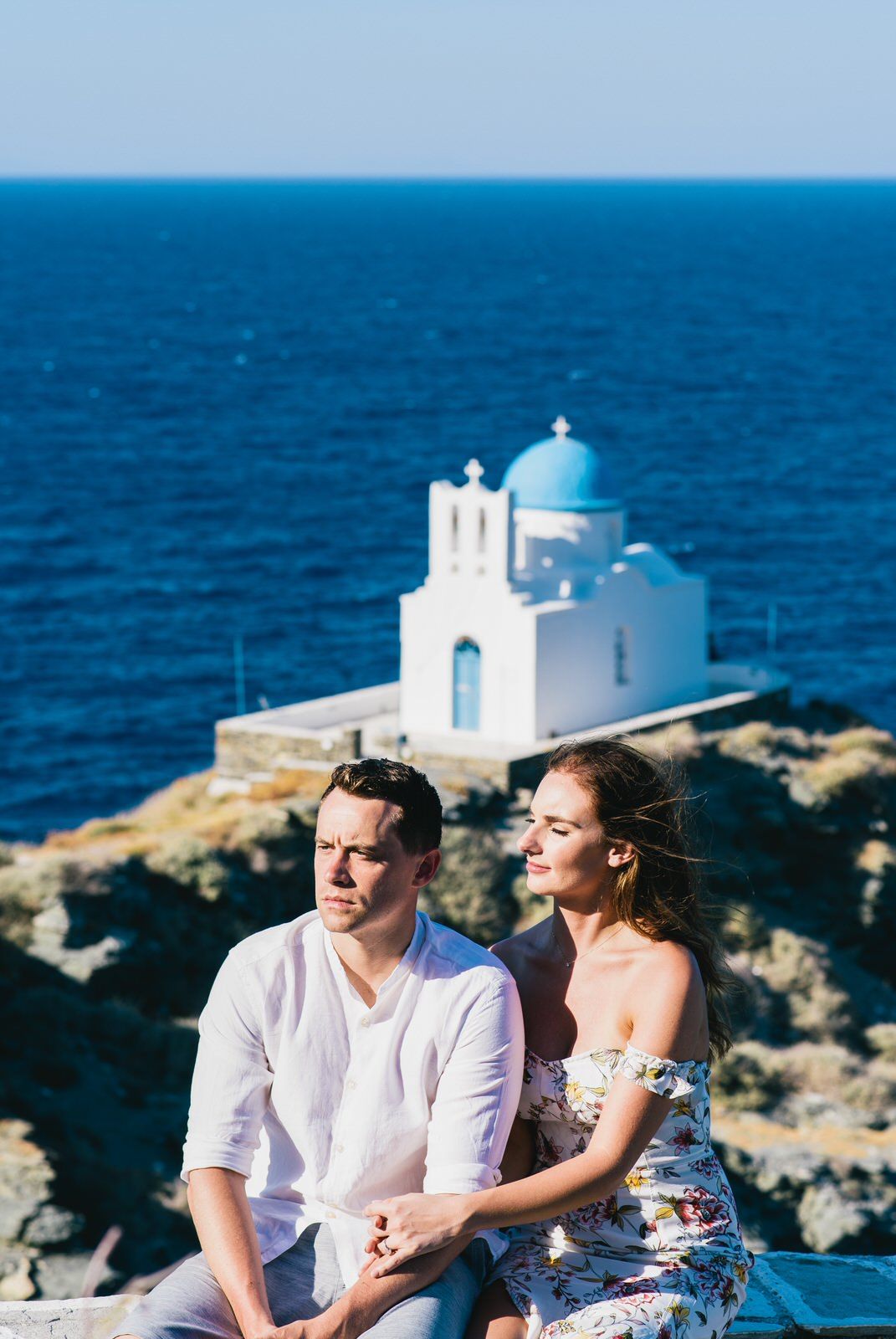 Couple near traditional white and blue Greek church overlooking the Mediterranean Sea.