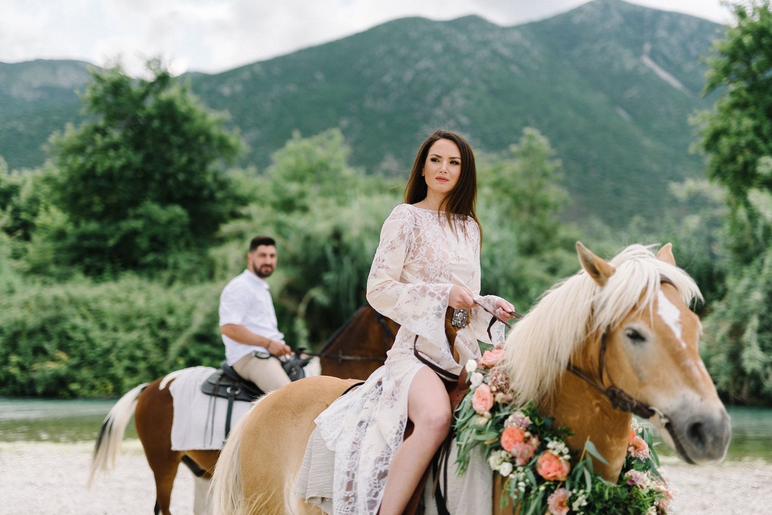Couple horseback riding through scenic mountain landscape with decorated horses.