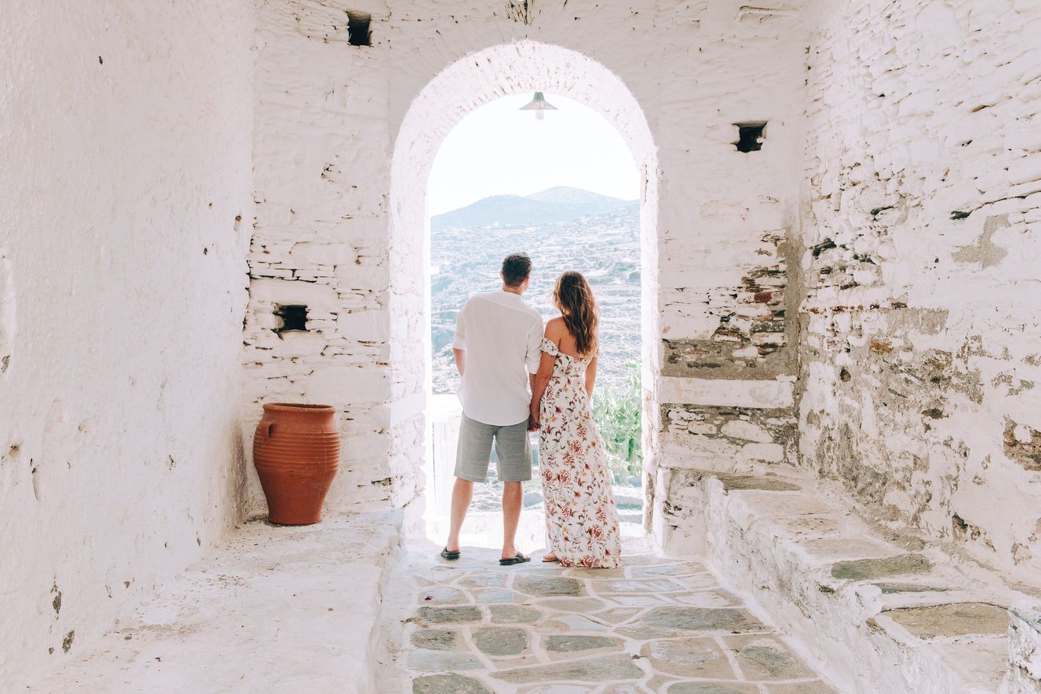 A couple standing in a rustic white doorway with ocean views and traditional Mediterranean architecture.