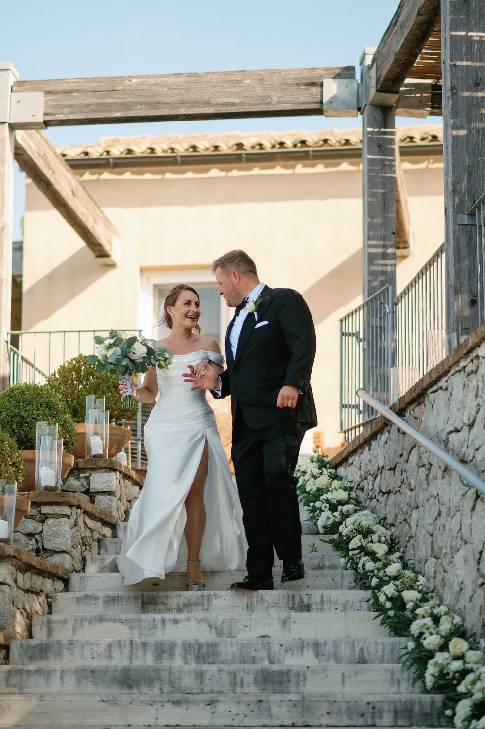 A romantic wedding moment on stone steps adorned with white flowers at a Mediterranean villa.