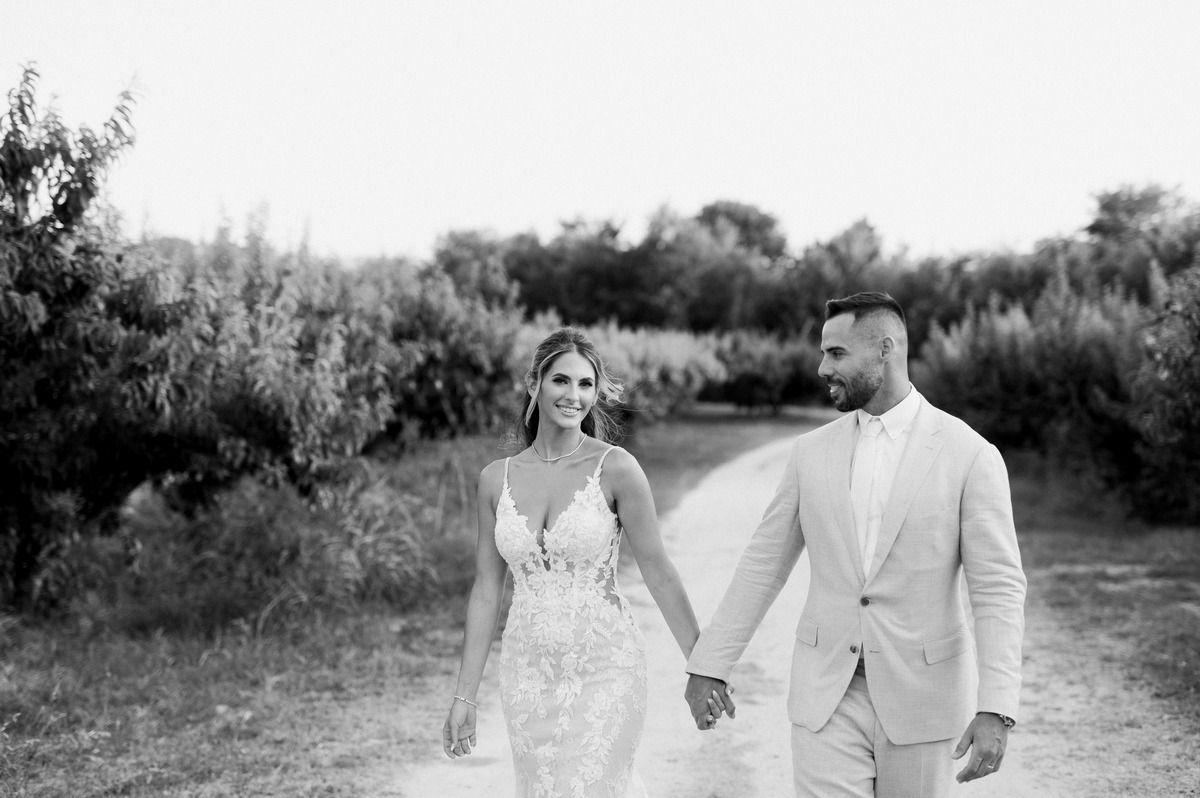 A couple walks hand in hand through a natural outdoor setting in formal wedding attire.