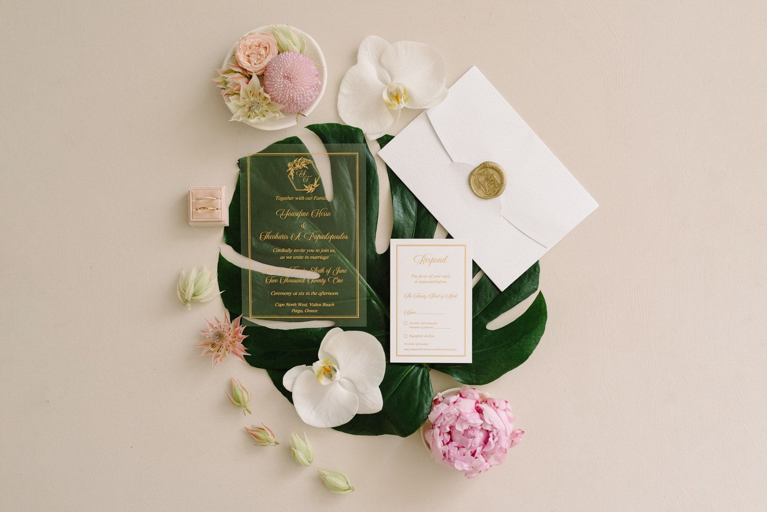 Wedding invitation suite with green and gold details arranged with white orchids and pink flowers.
