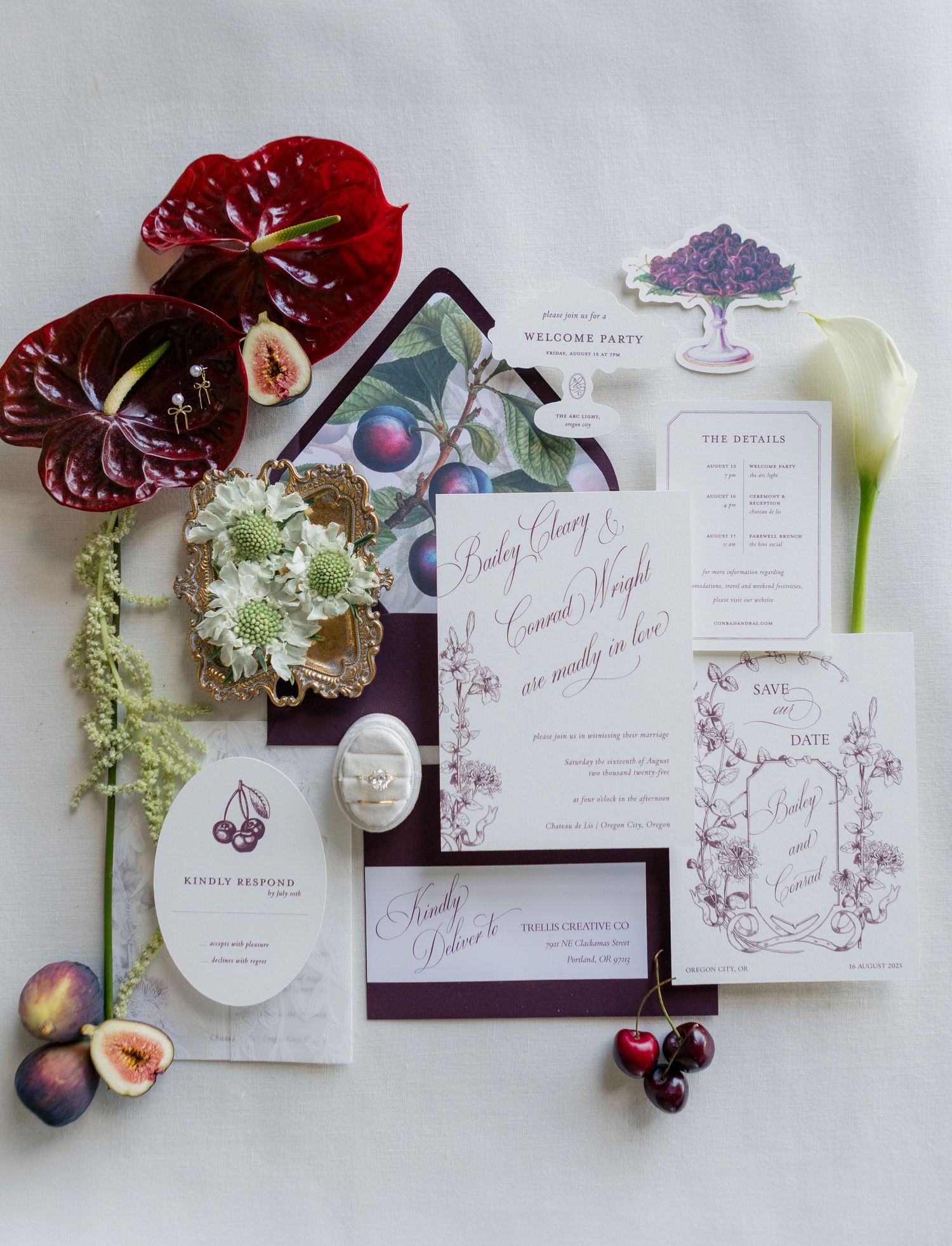 Wedding invitation suite with burgundy floral designs, anthurium flowers and peach accents laid flat on white background.
