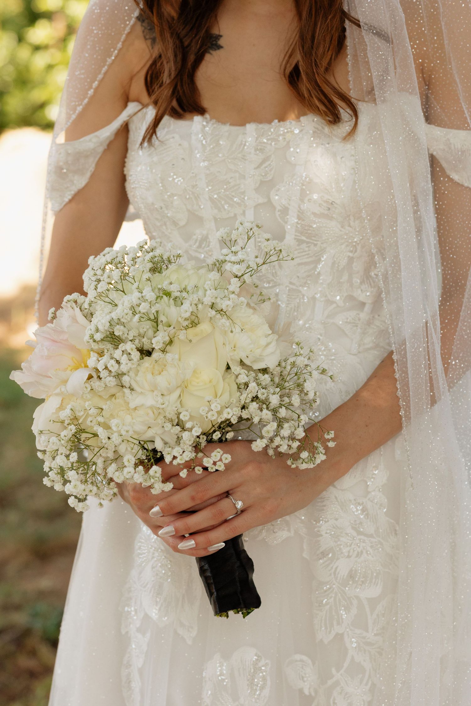 Bride in white lace gown holding elegant bouquet of white roses and baby's breath on wedding day.
