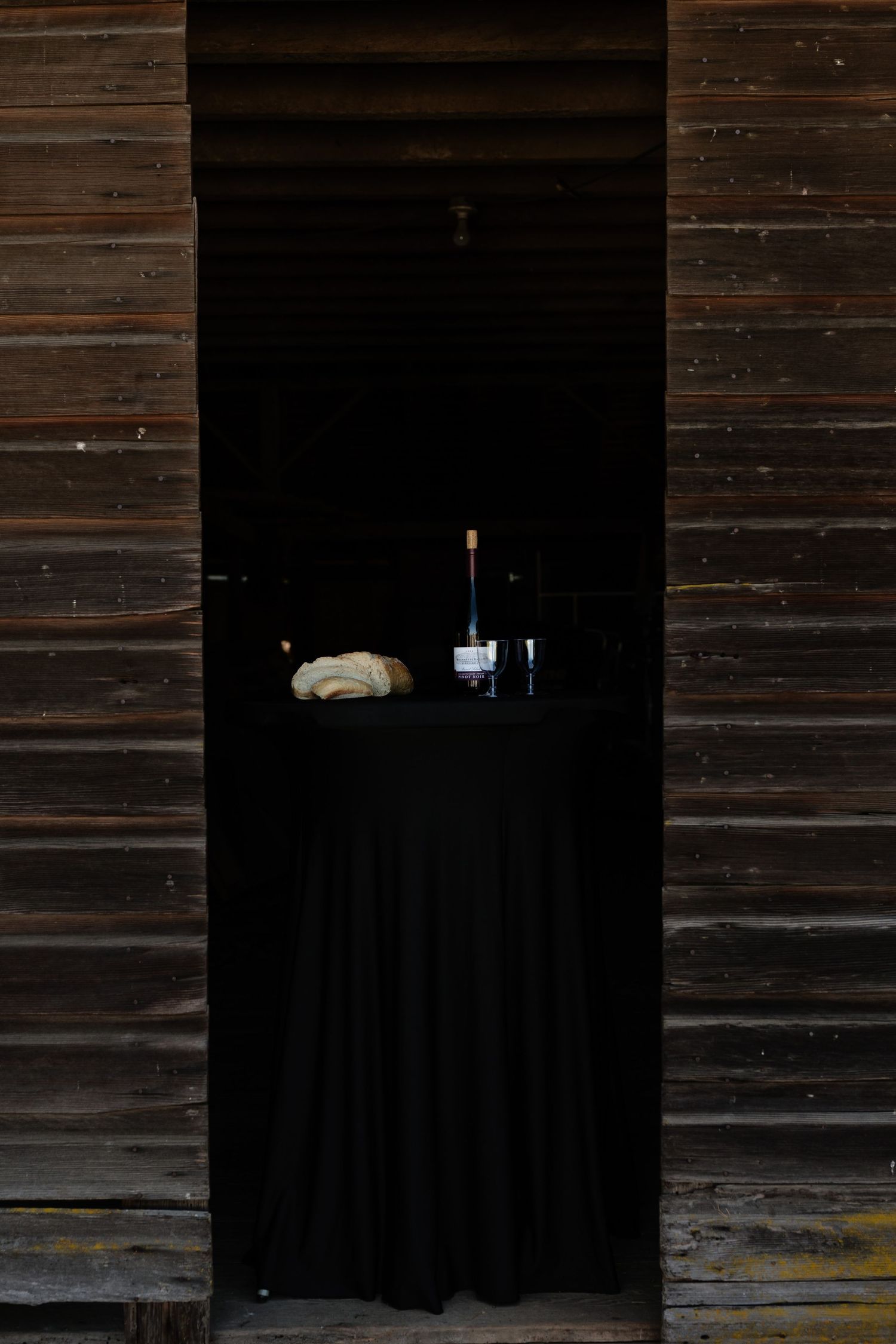 Black draped table with champagne bottle and bread displayed in rustic barn doorway wedding setup.