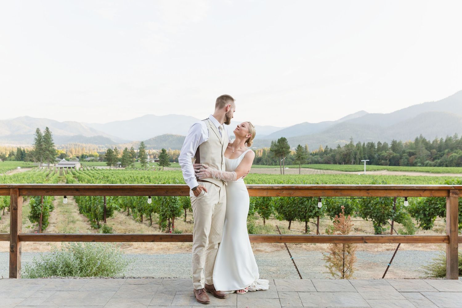 A couple shares an intimate moment on a winery terrace overlooking scenic vineyard rows and mountains.