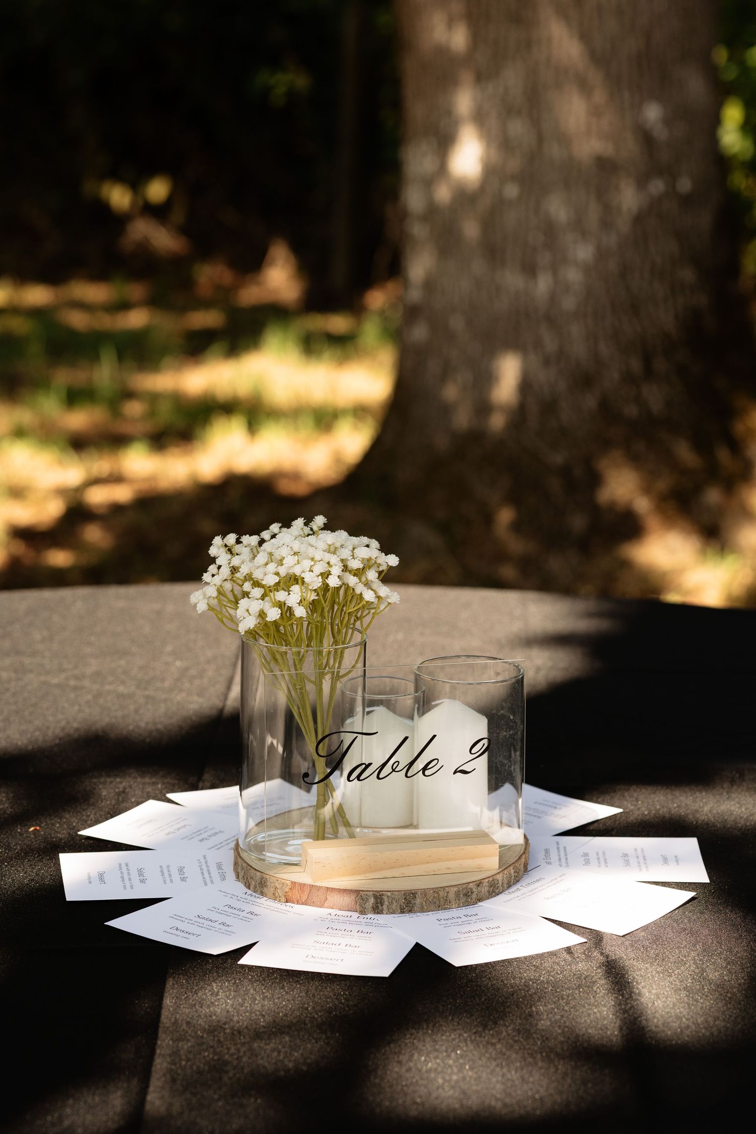 Elegant outdoor wedding table centerpiece with baby's breath, candle, and Table 2 sign on wood slice.