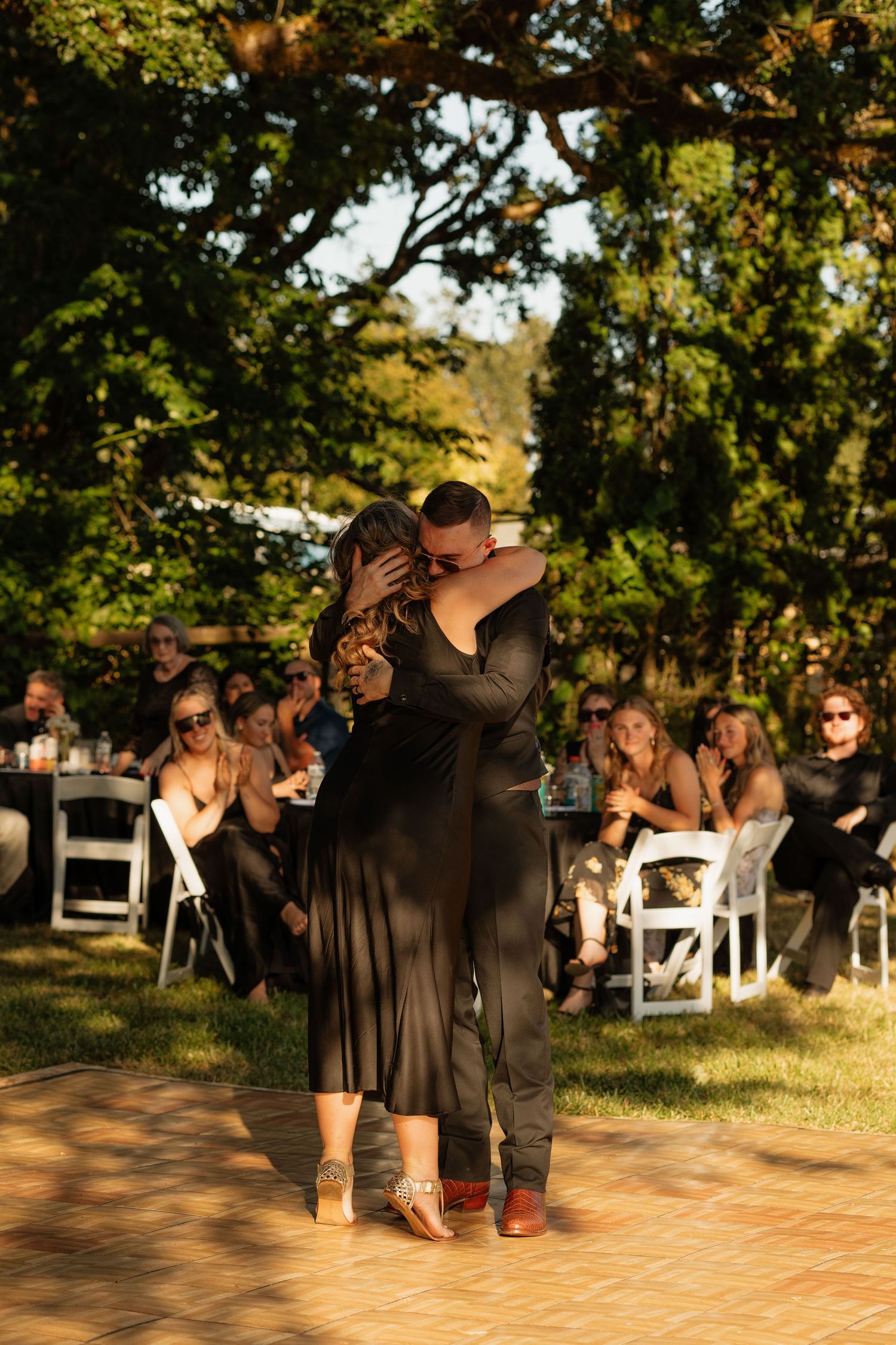 Couple sharing an intimate dance at an outdoor wedding reception surrounded by guests seated at white chairs.