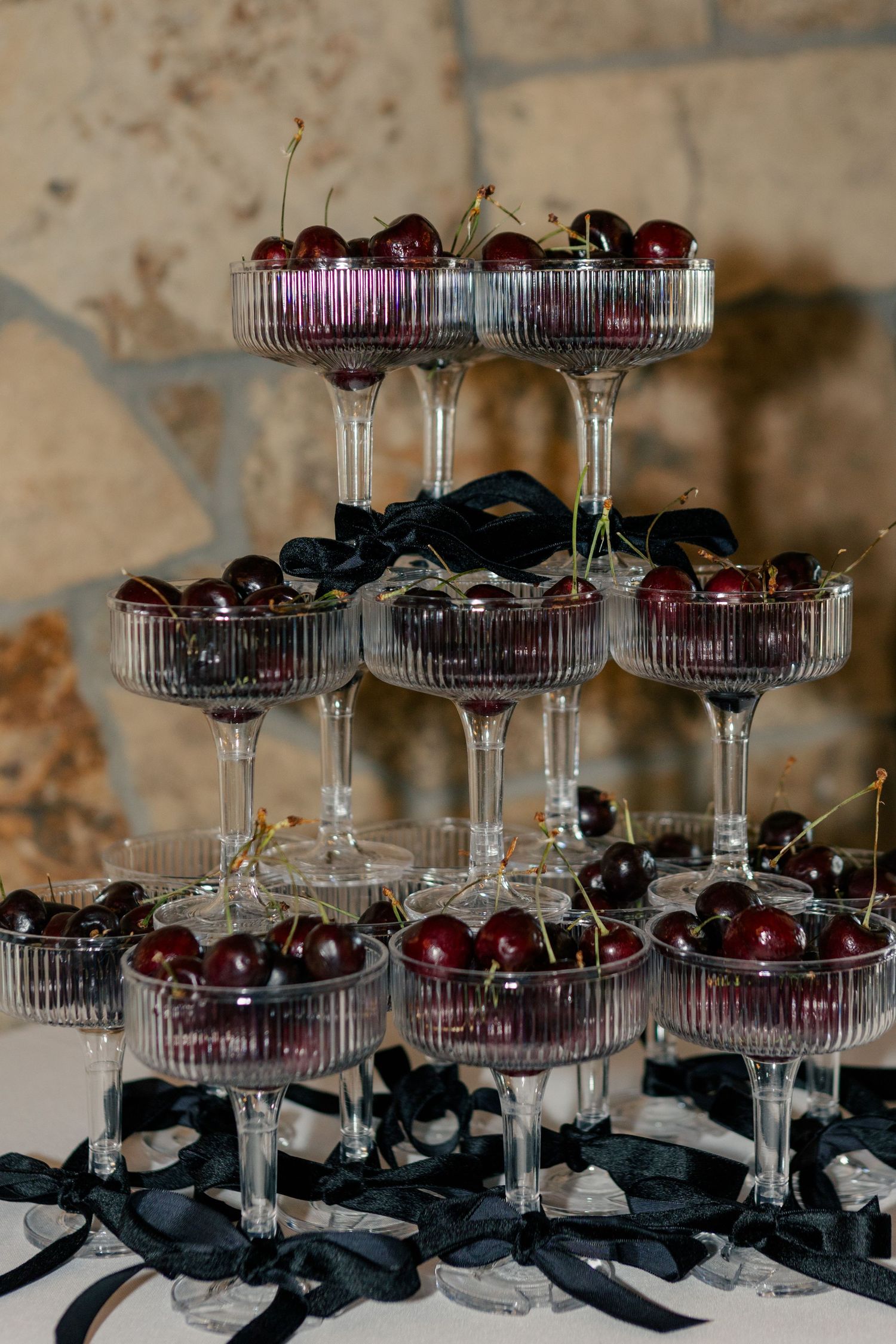 Elegant champagne flutes arranged in tiers display fresh dark cherries with black ribbon accents for a sophisticated event.