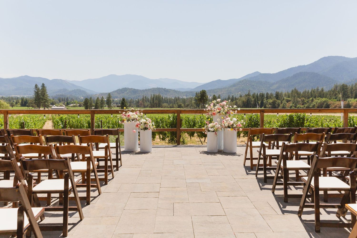 Rustic wooden chairs set up for an outdoor wedding ceremony with mountain ranges and evergreen forests in the backdrop.