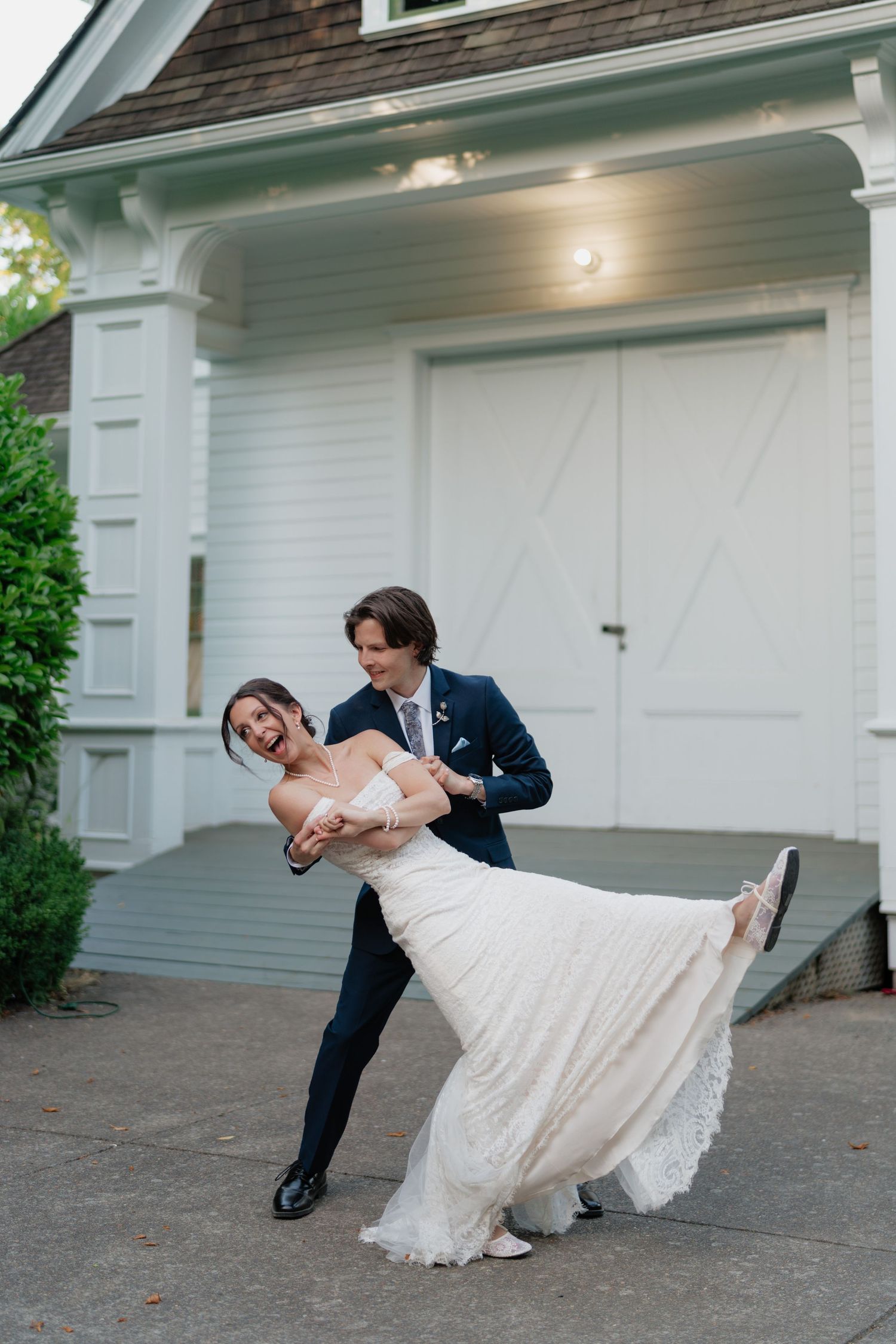 Groom dips bride in elegant dance pose outside white building at wedding reception.