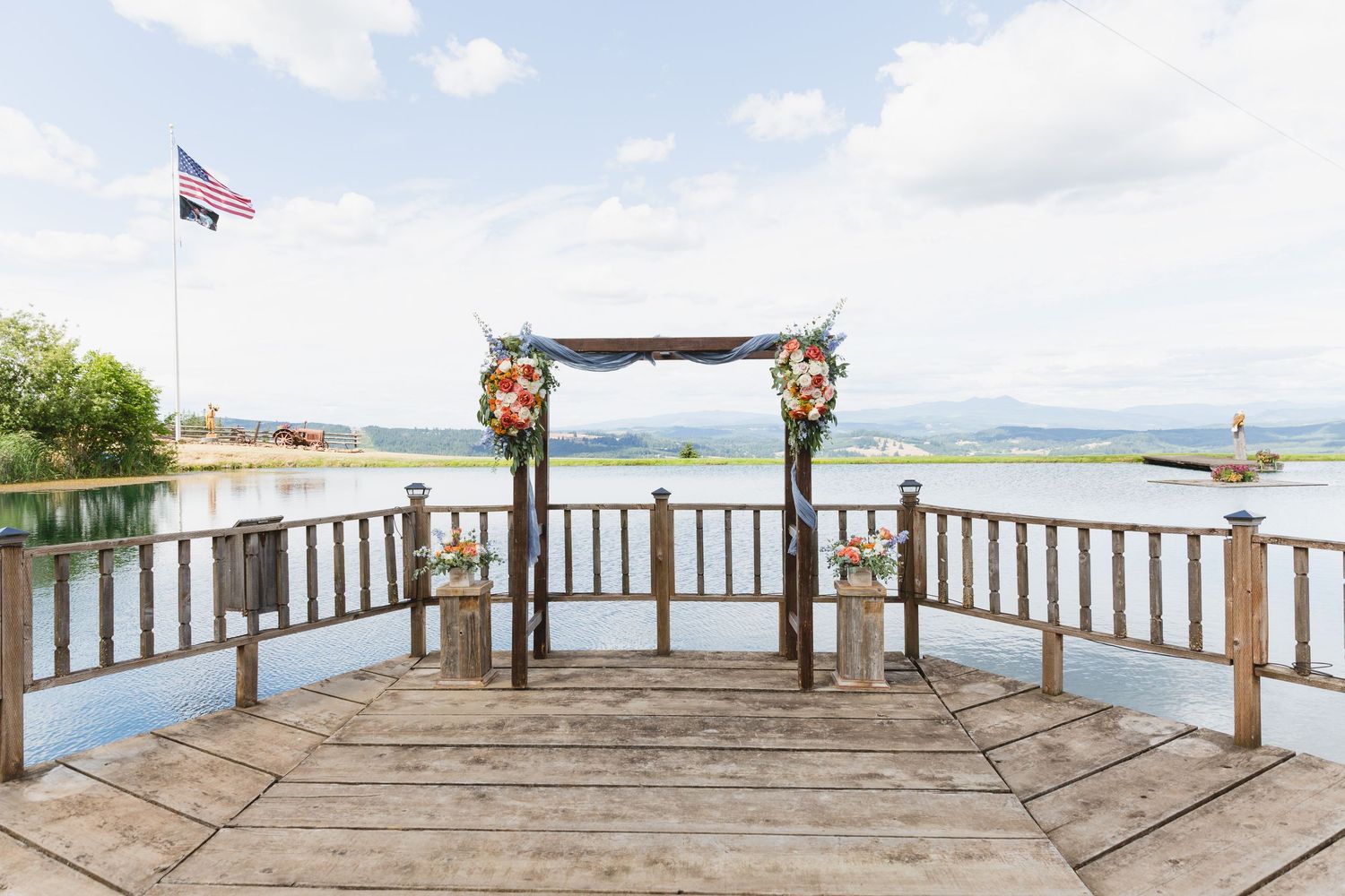Wooden seaside wedding arch decorated with flowers on a circular deck overlooking ocean waters and mountains.