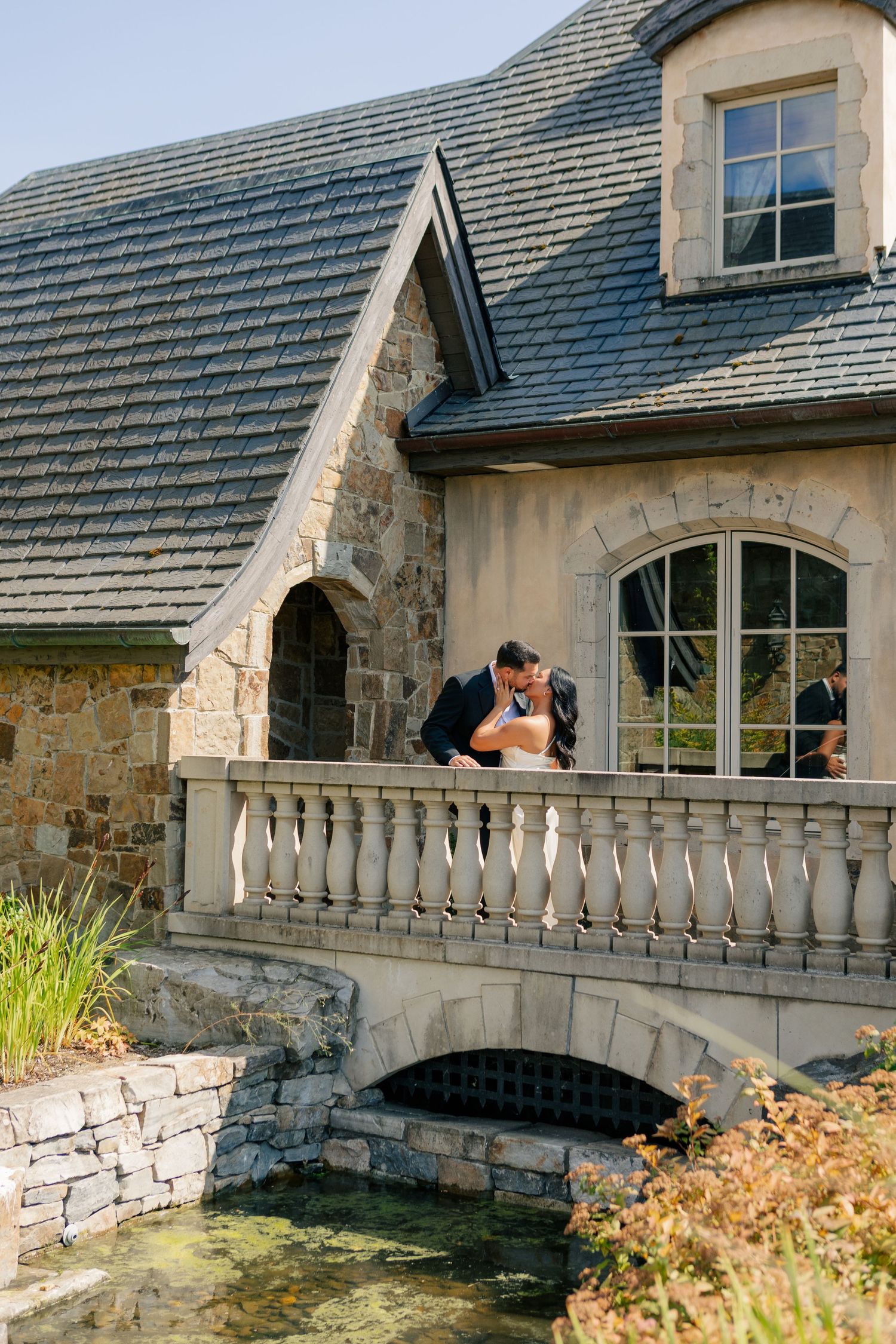 Stone balcony with decorative balustrade extends along the exterior of a stately home on a sunny day.