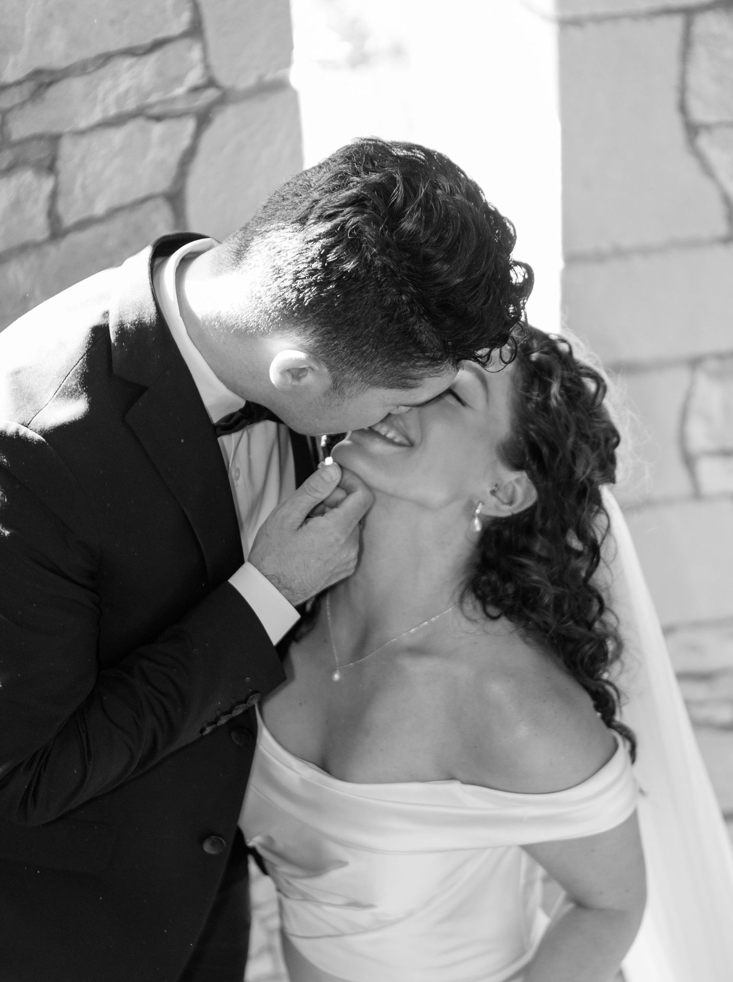 A black and white photo sequence shows a couple sharing a tender kiss in front of a white brick wall.
