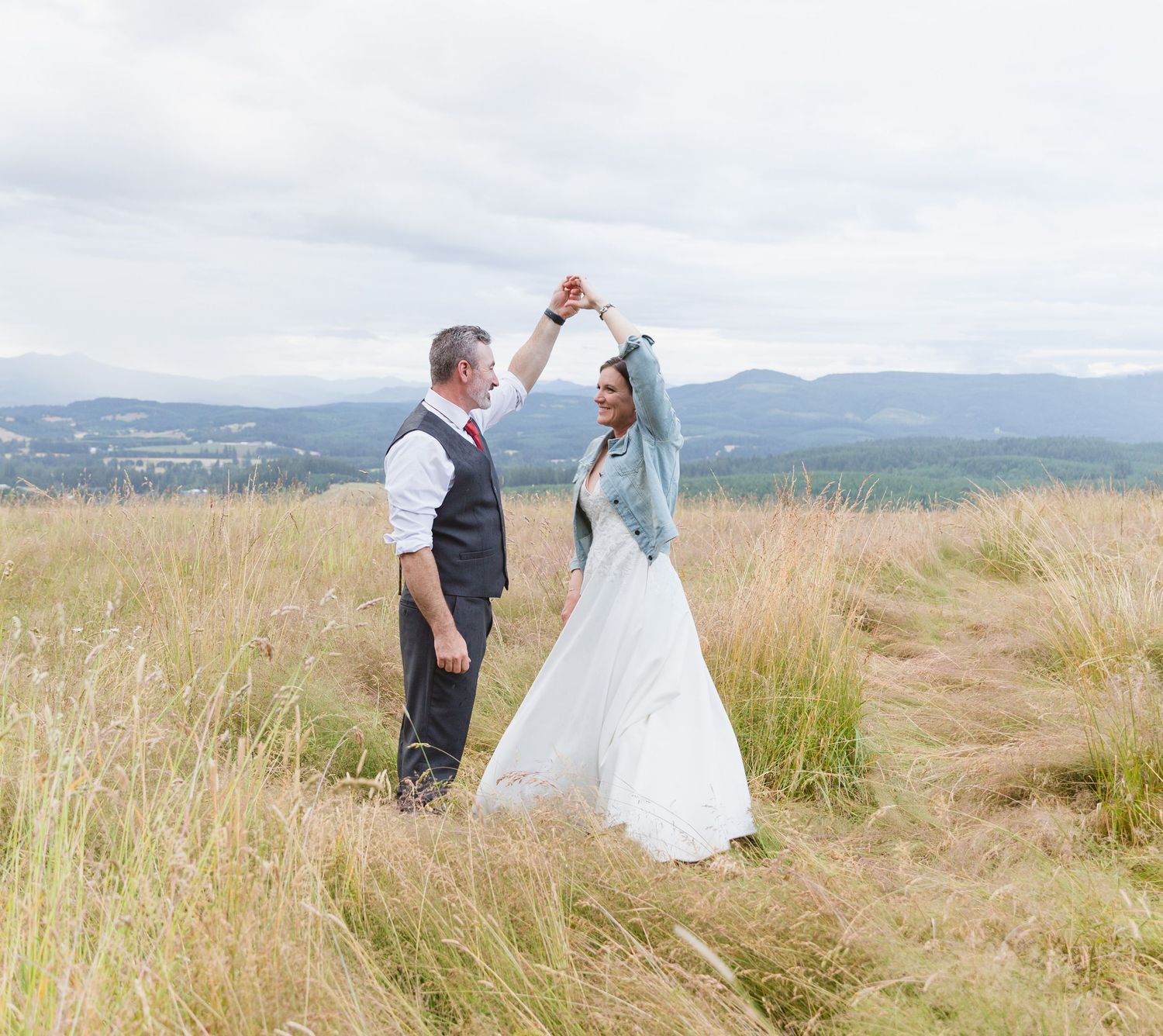 Newlyweds celebrating in a scenic field of tall grass with mountain views in the background.