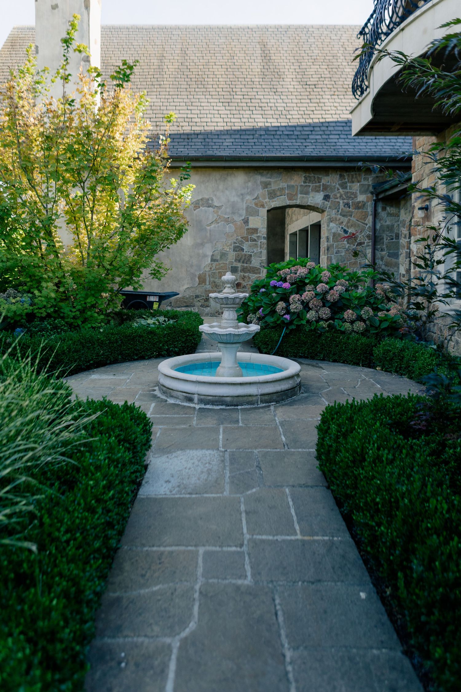 Stone paved garden path leading to a decorative fountain surrounded by manicured hedges and greenery.