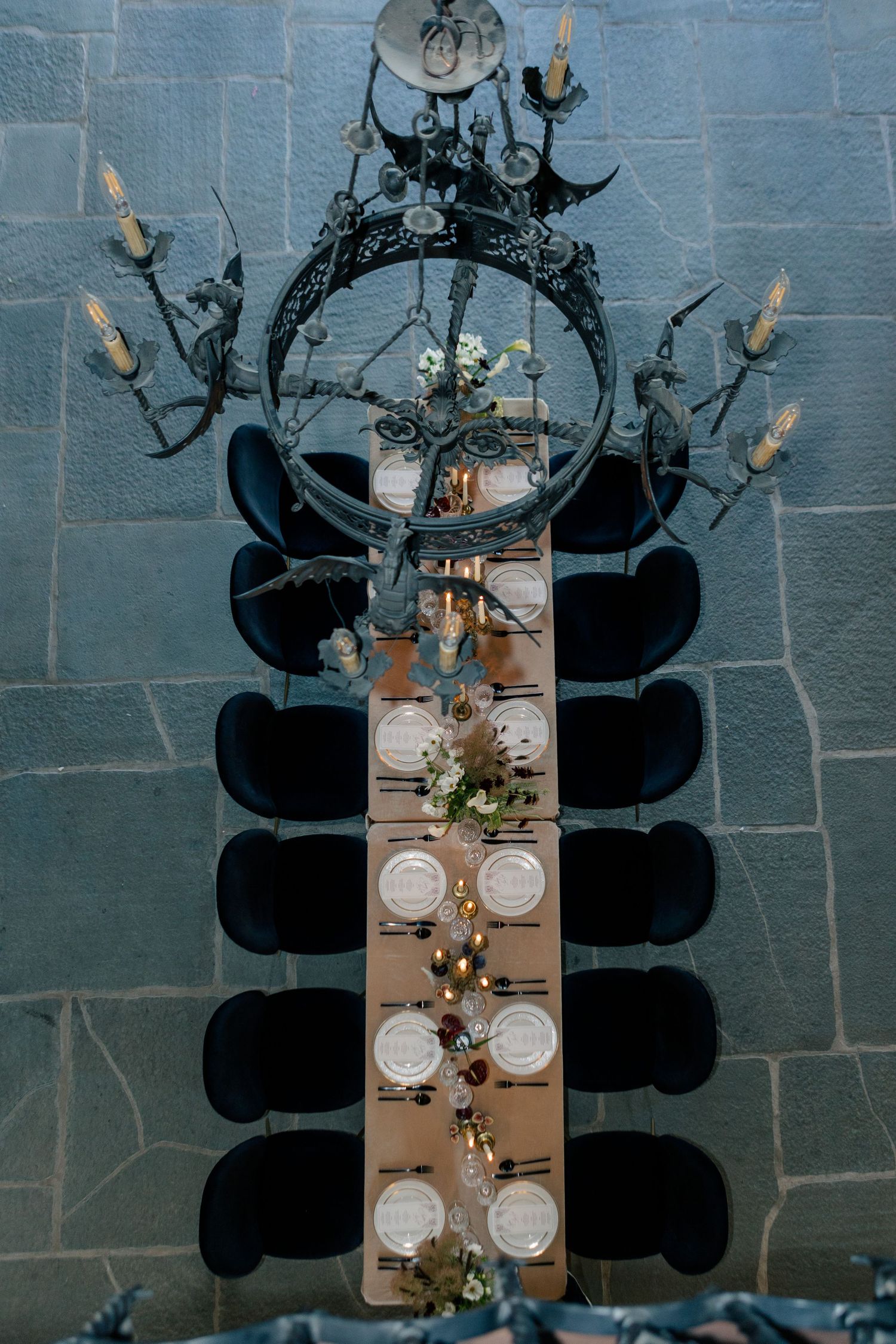 Overhead view of an elegant dining table arrangement with place settings against a dark blue wall casting dramatic shadows.