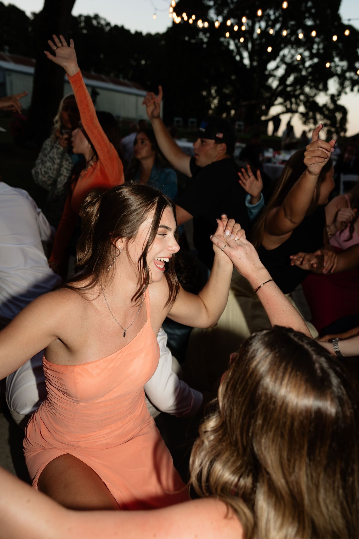 Guests dancing joyfully at outdoor wedding reception under string lights at dusk.