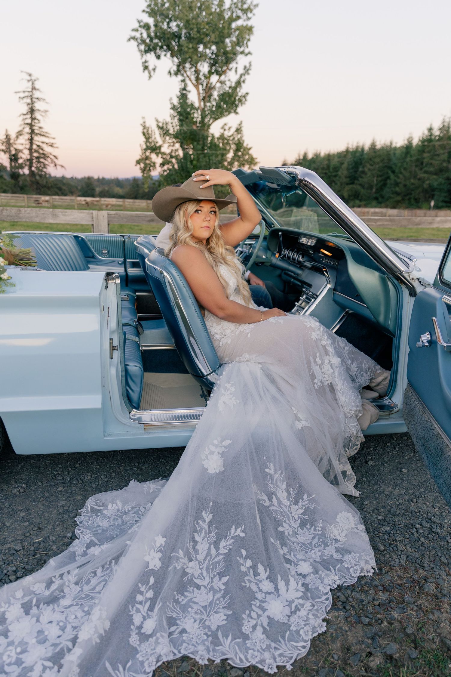 A classic convertible features flowing white lace wedding dress details with a sunset forest backdrop.