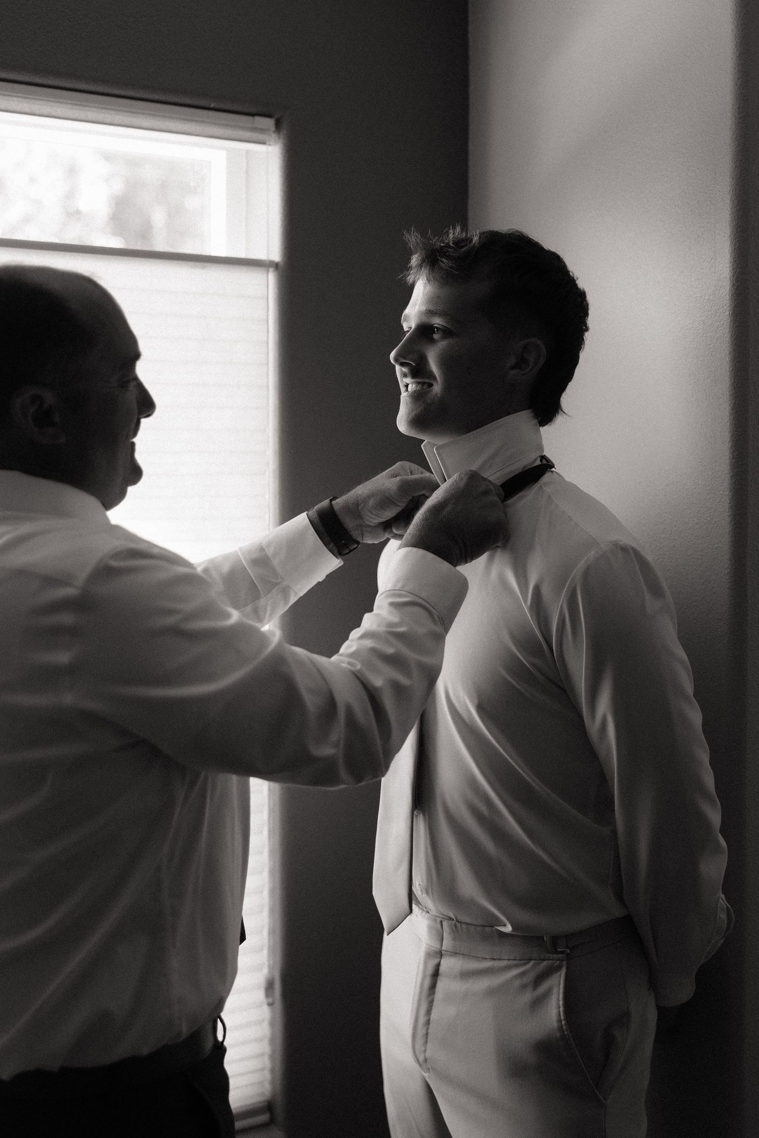 Black and white photo of groomsman helping groom adjust bow tie before wedding ceremony.