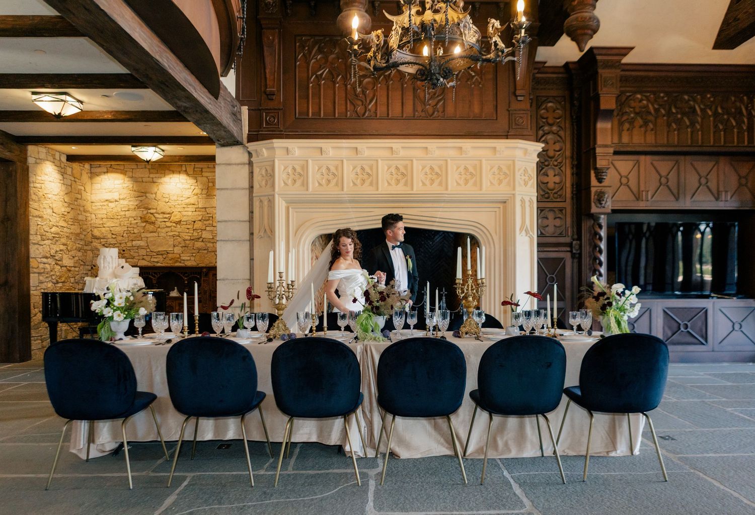 Elegant ballroom venue with dark blue chairs, chandeliers, and draped tables set for a formal dining event.