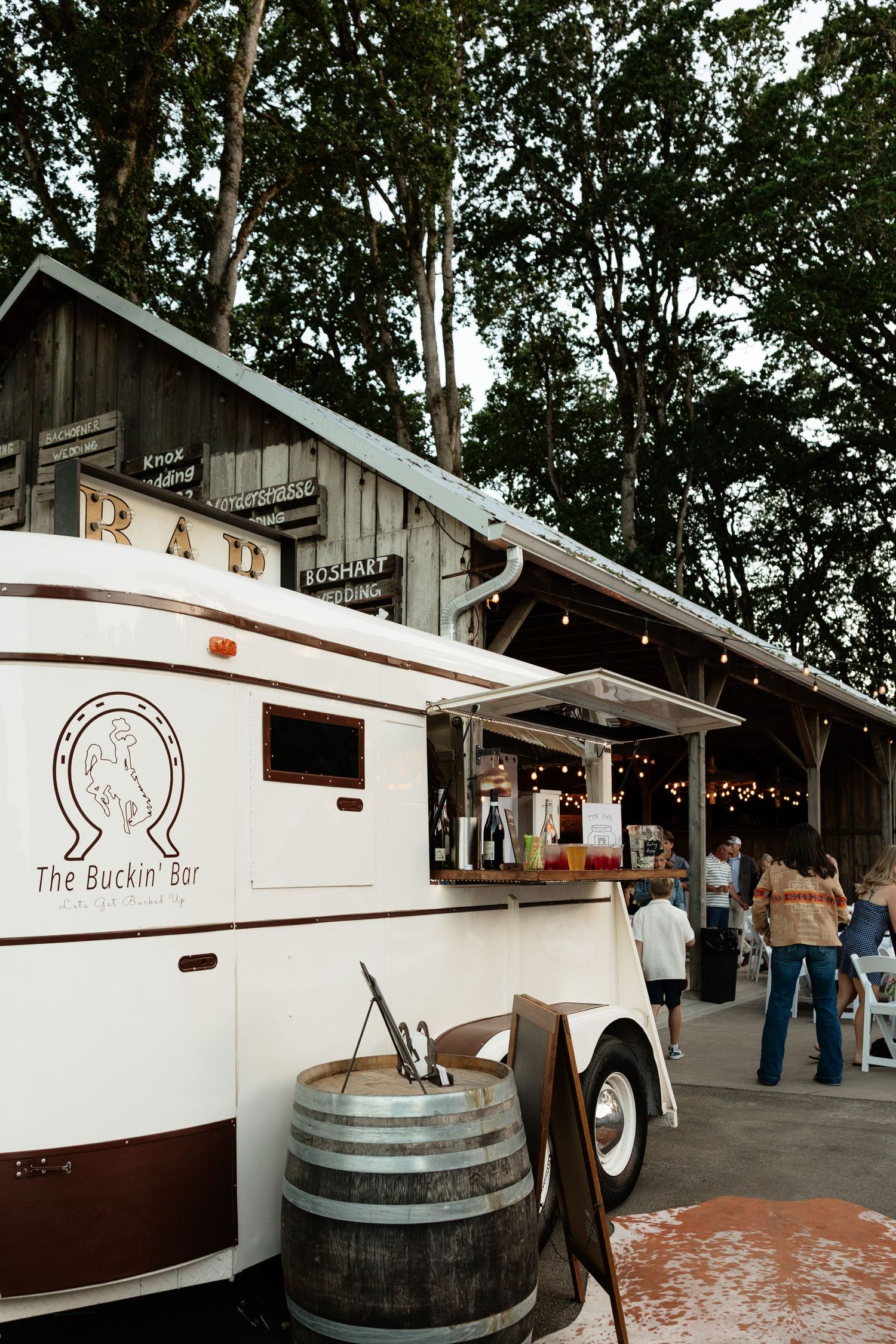 The Buckin' Bar mobile bar truck with wine barrel outside a rustic barn venue at an outdoor event.