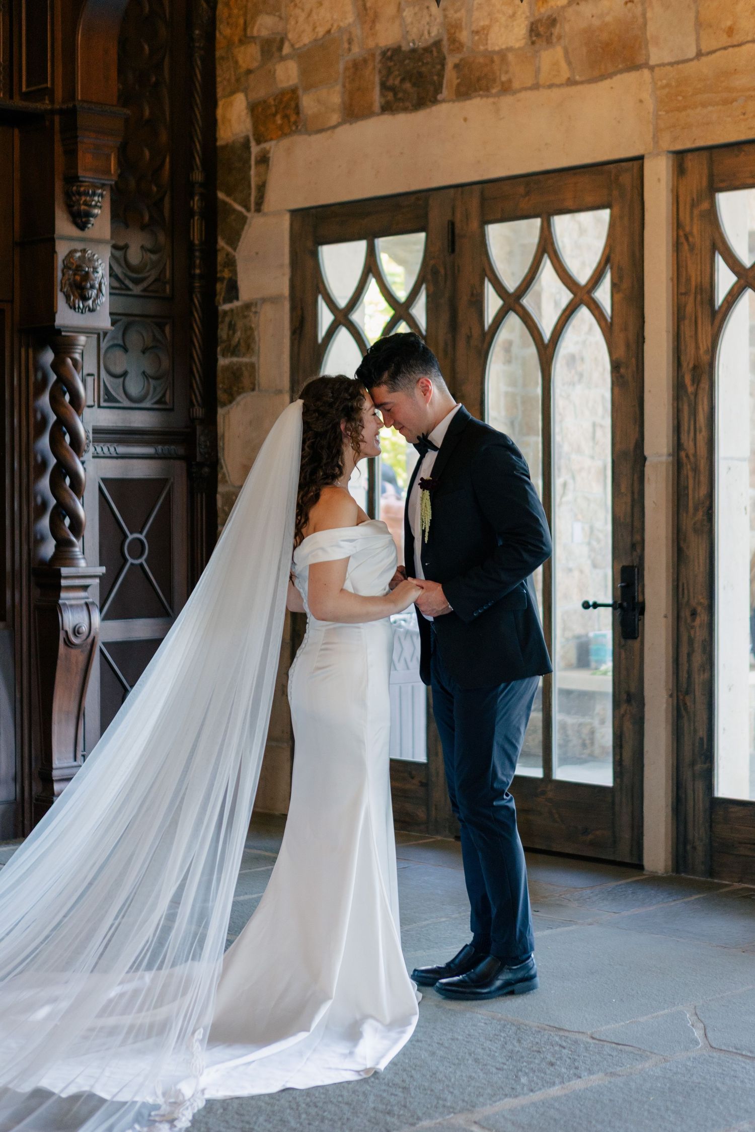 A romantic moment captured in an elegant stone hallway with arched gothic windows and flowing white veil.