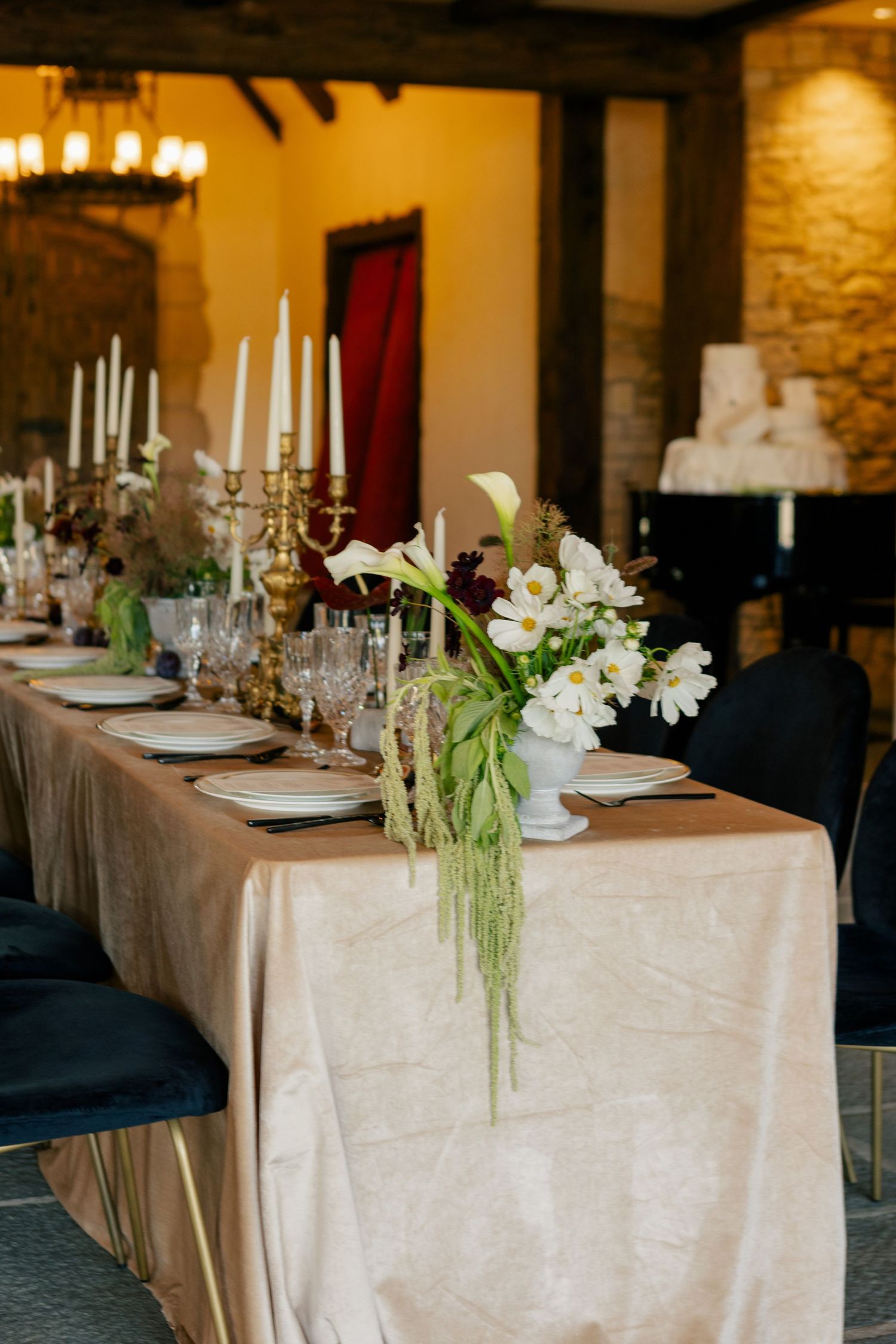 Elegant wedding reception table setting with white linens, floral centerpieces, and crystal candlesticks in a rustic stone room.