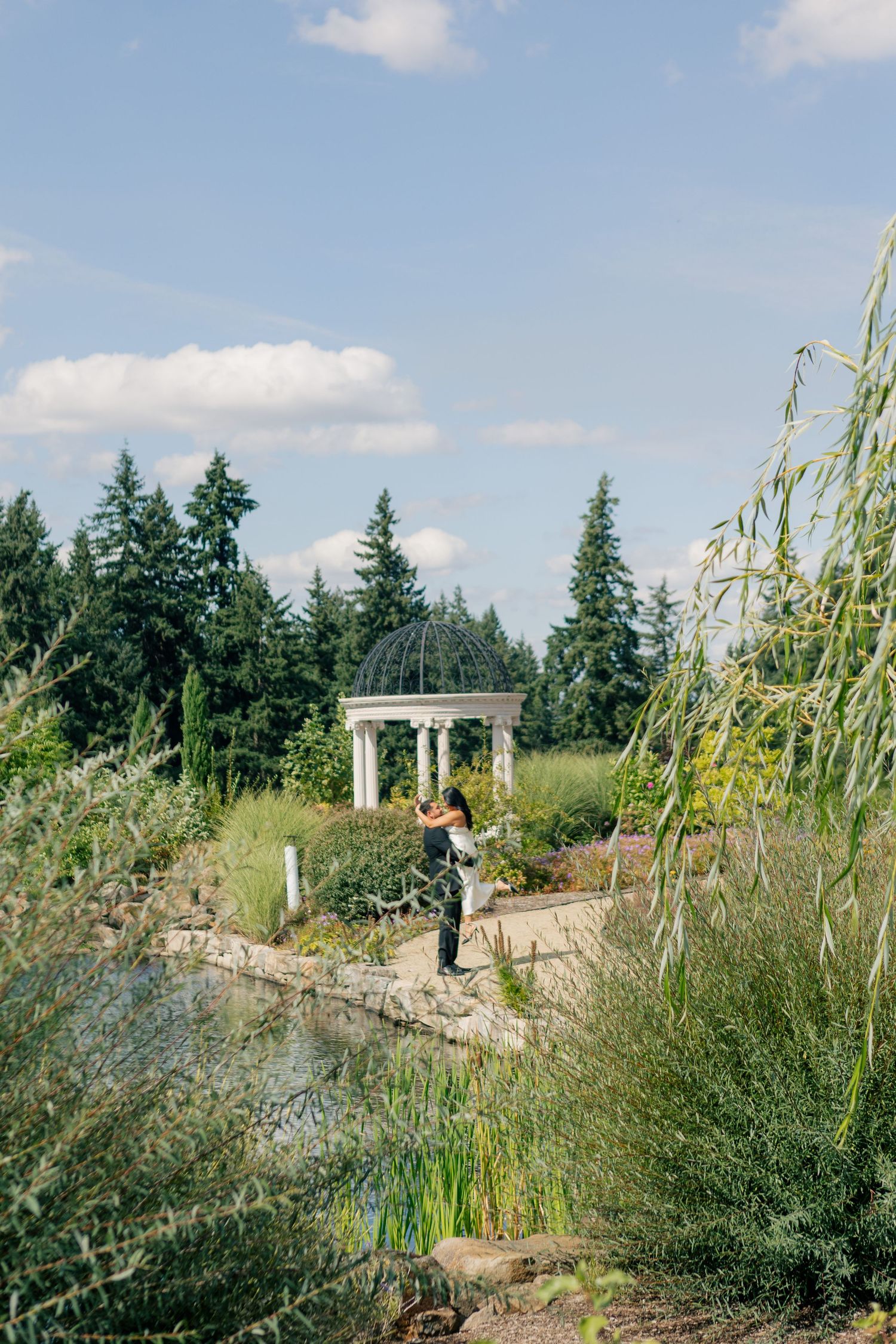 Stone pathway leads through a tranquil garden with ornamental grass and decorative gazebo in the distance.