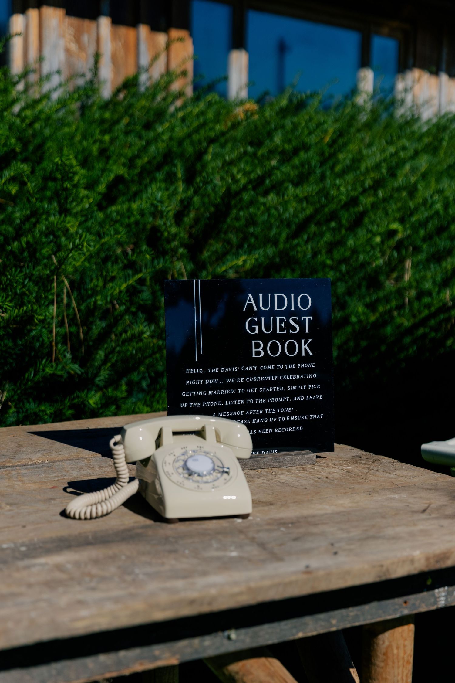 Guest book and audio guide signage displayed on a rustic wooden table outdoors.