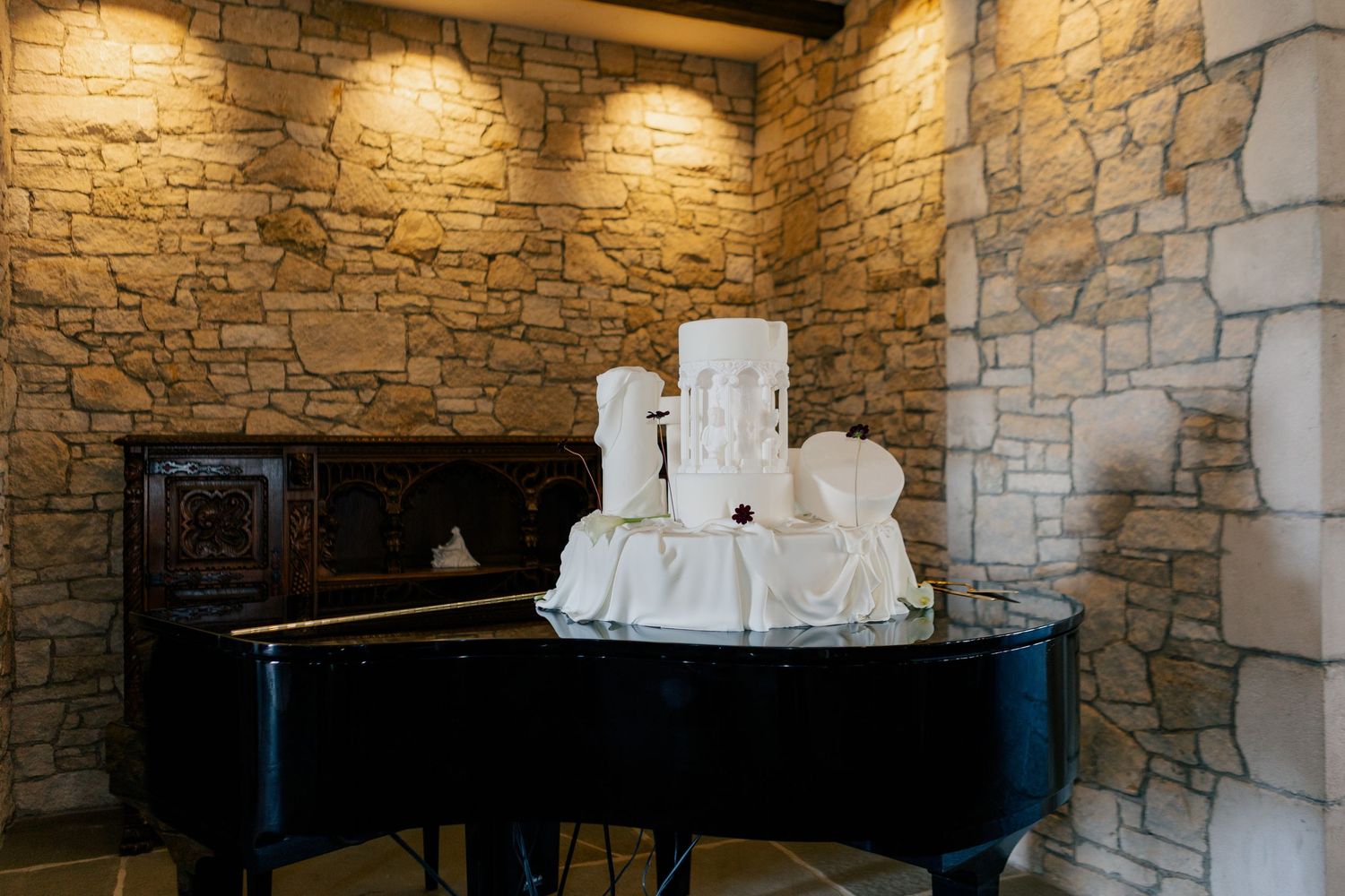 Long banquet table with place settings and white floral arrangements against a textured stone wall with warm lighting.